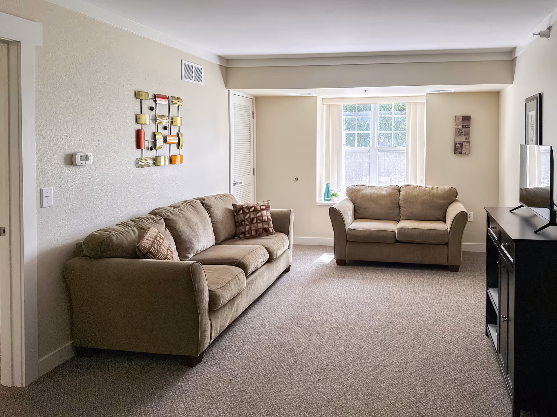 Cozy beige living room in a senior facility with two sofas, wall art, and TV stand.