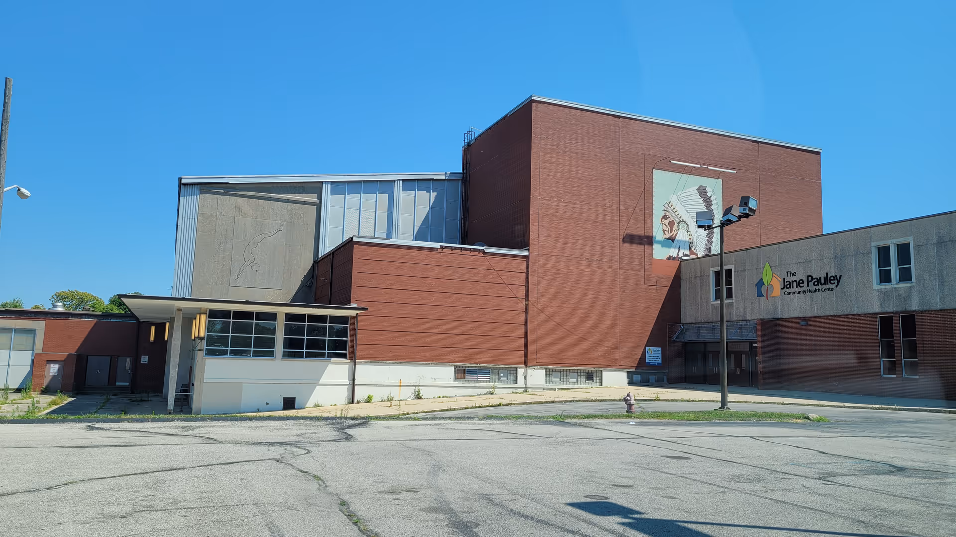 Exterior view of a brick building with a mural and sign under blue sky.