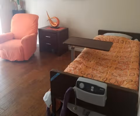 A bedroom with an adjustable bed, orange bedding, a chair, and a nightstand.