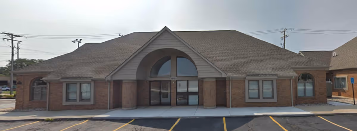 Exterior view of a brick senior care facility with arched entrance and empty parking lot.