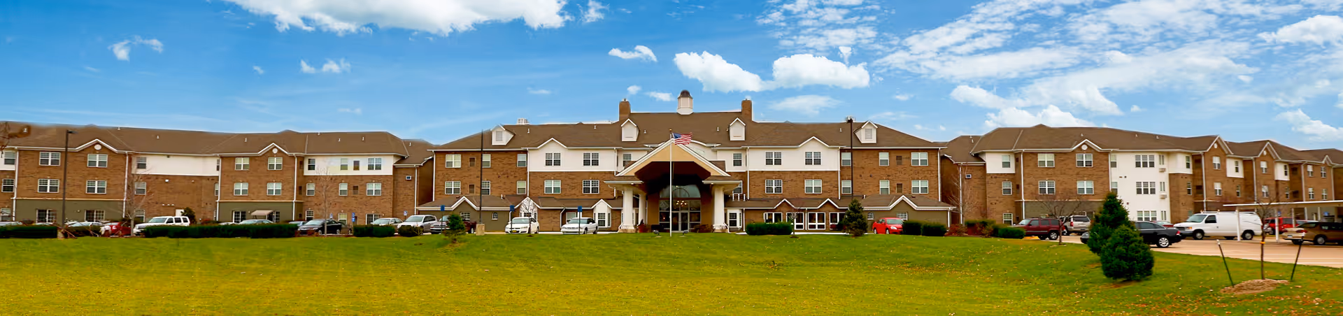 Wide exterior view of Reflection Ridge senior living facility with brick facade and green lawn.