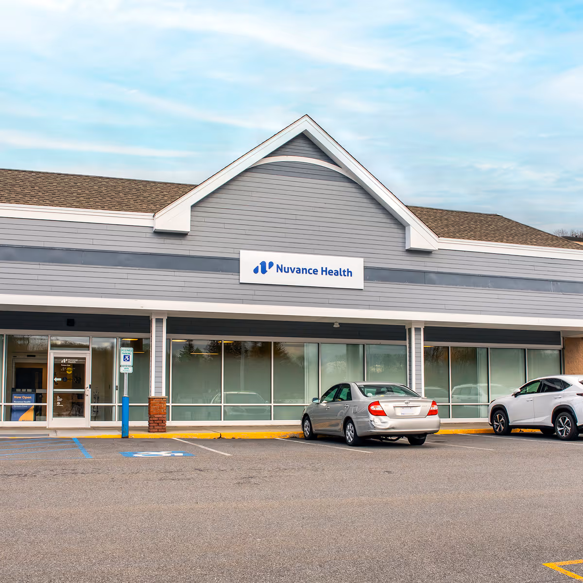 Exterior view of a Nuvance Health facility with glass windows and parked cars.