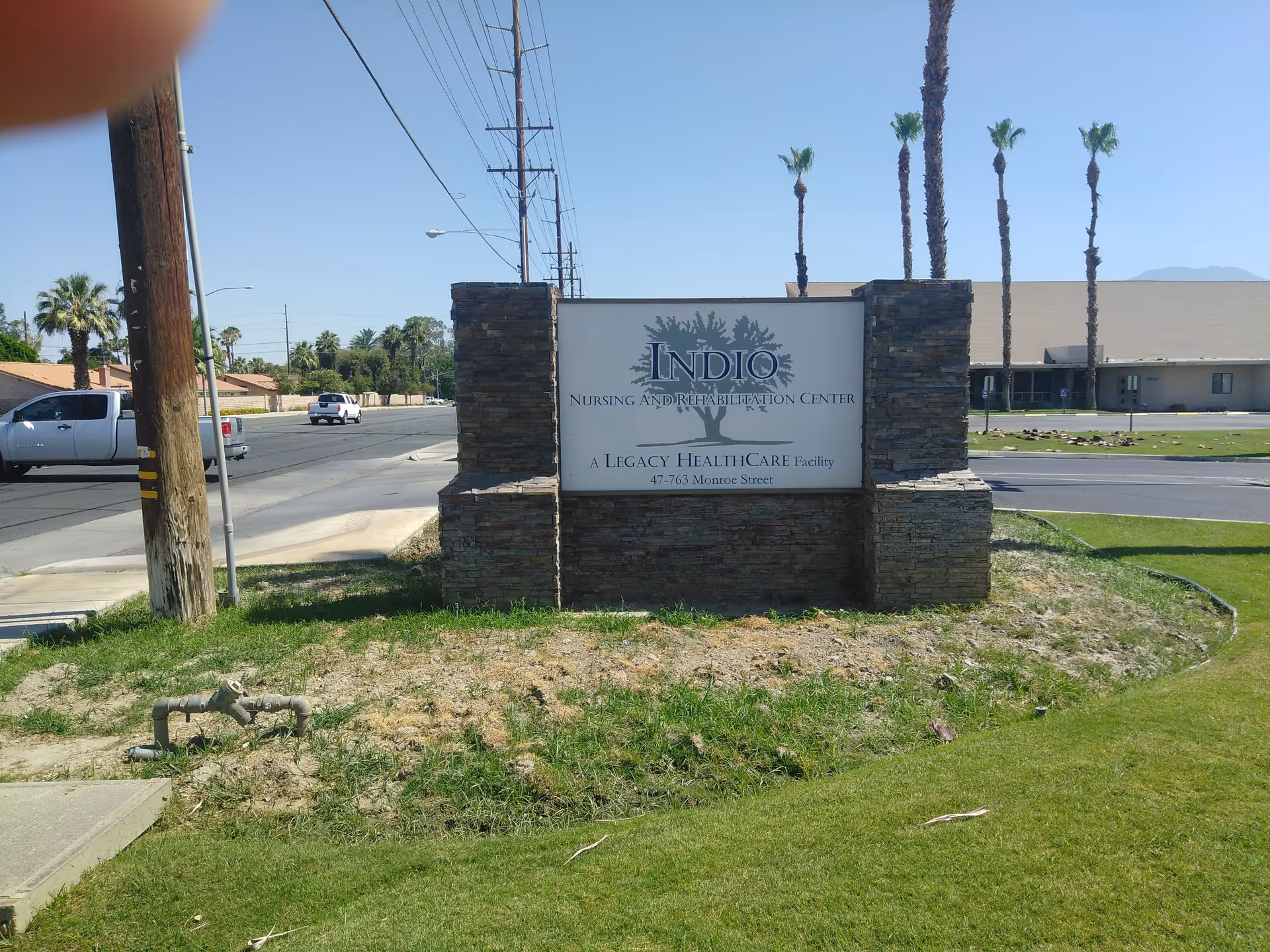Outdoor street view of a stone sign reading Indio Nursing & Rehabilitation Center in desert landscaping.