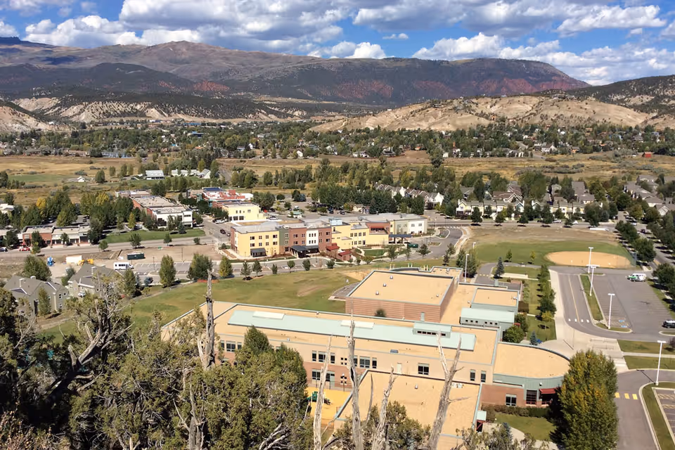 Aerial view of a large campus complex in a valley with surrounding town and mountains