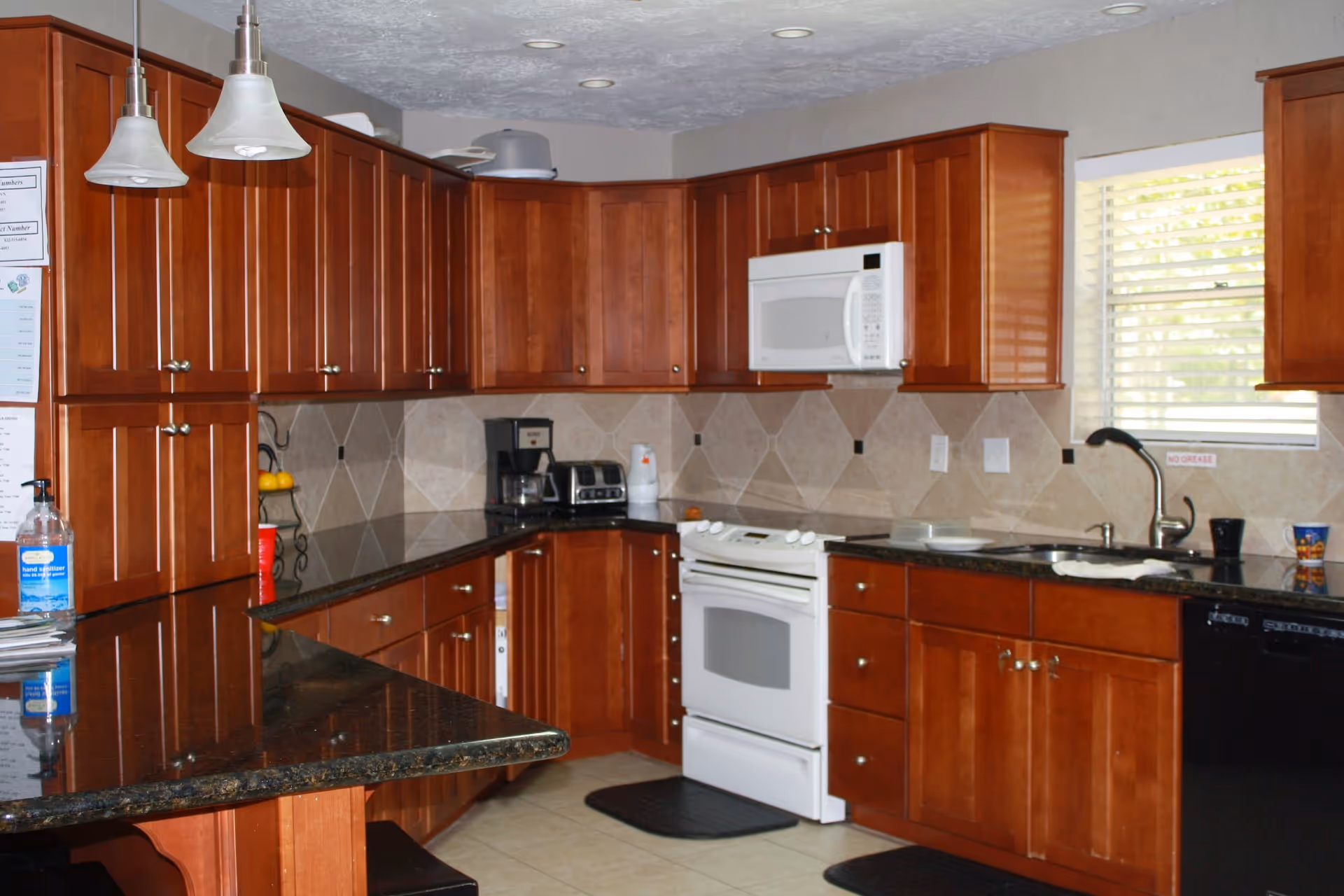 Compact kitchen with wooden cabinets, stove, microwave, sink, and granite countertops.