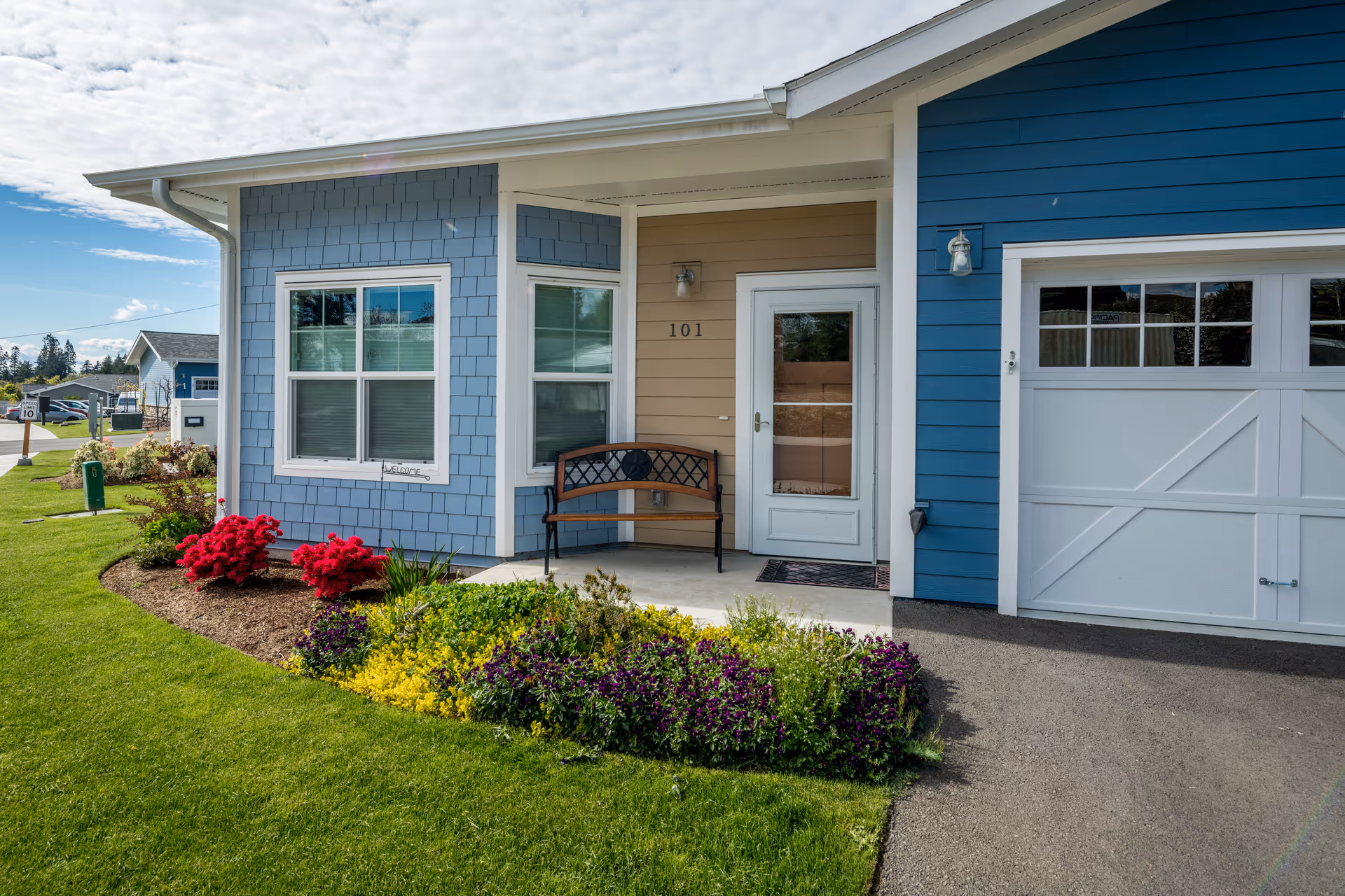 Front exterior of a blue Wesley Des Moines senior living building with garden and bench