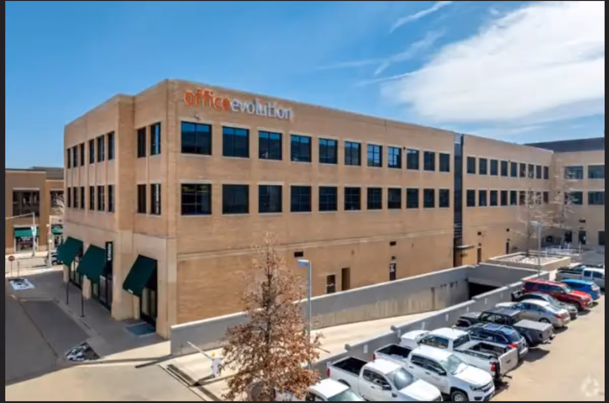 Exterior view of a tan brick building with a parking lot and storefronts