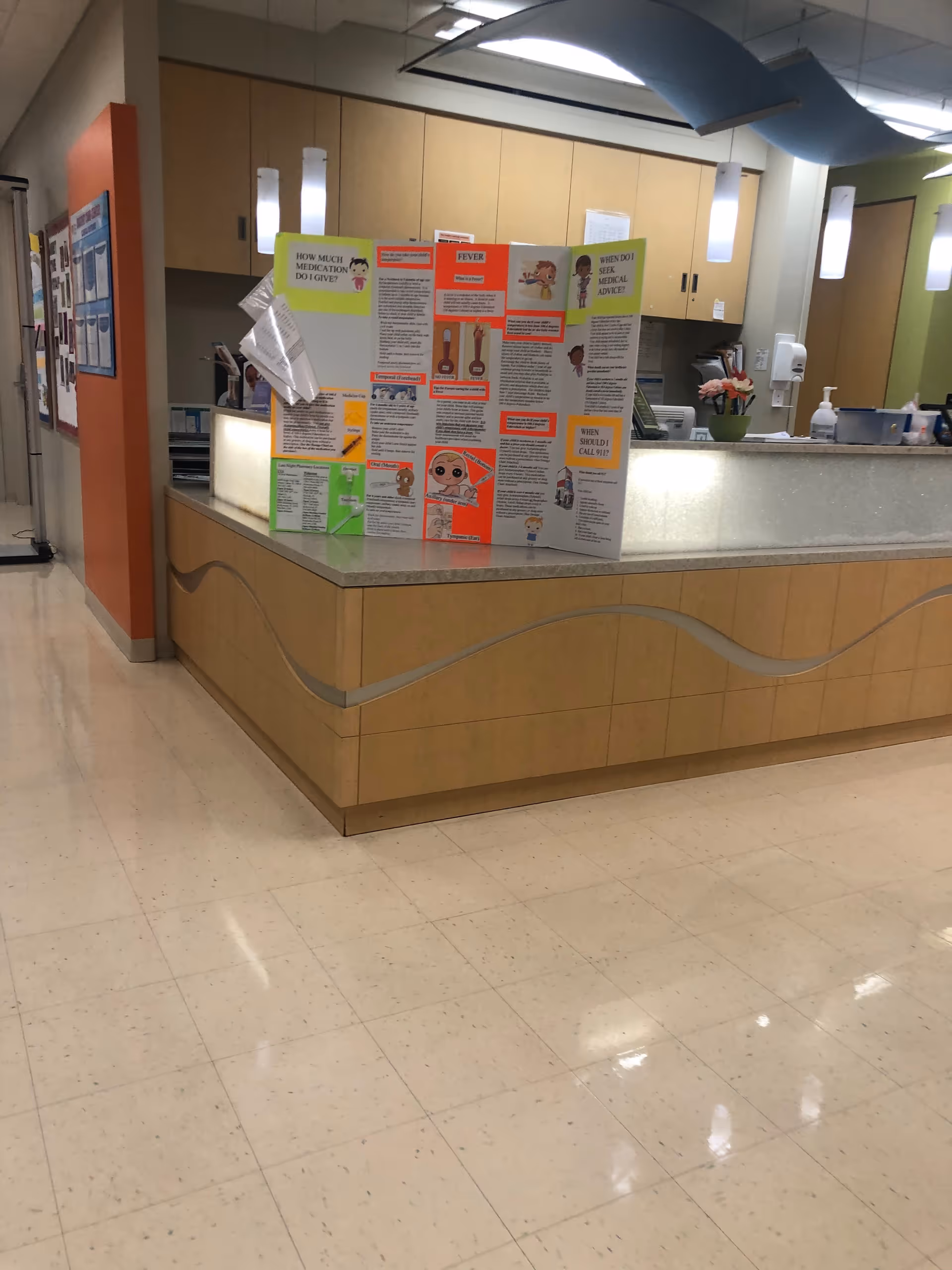 Indoor reception area with a curved wood desk and colorful bulletin board.