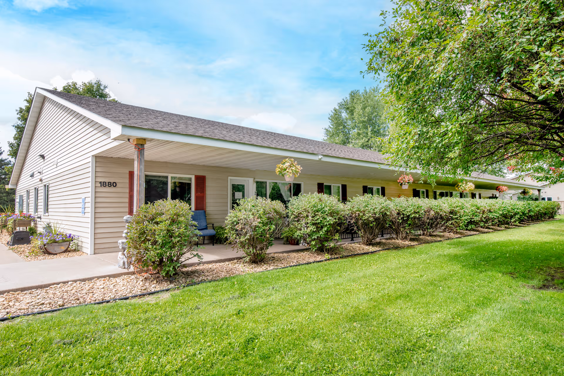 Comforts of Home Baldwin exterior with shrubs, lawn, and hanging planters along walkway.