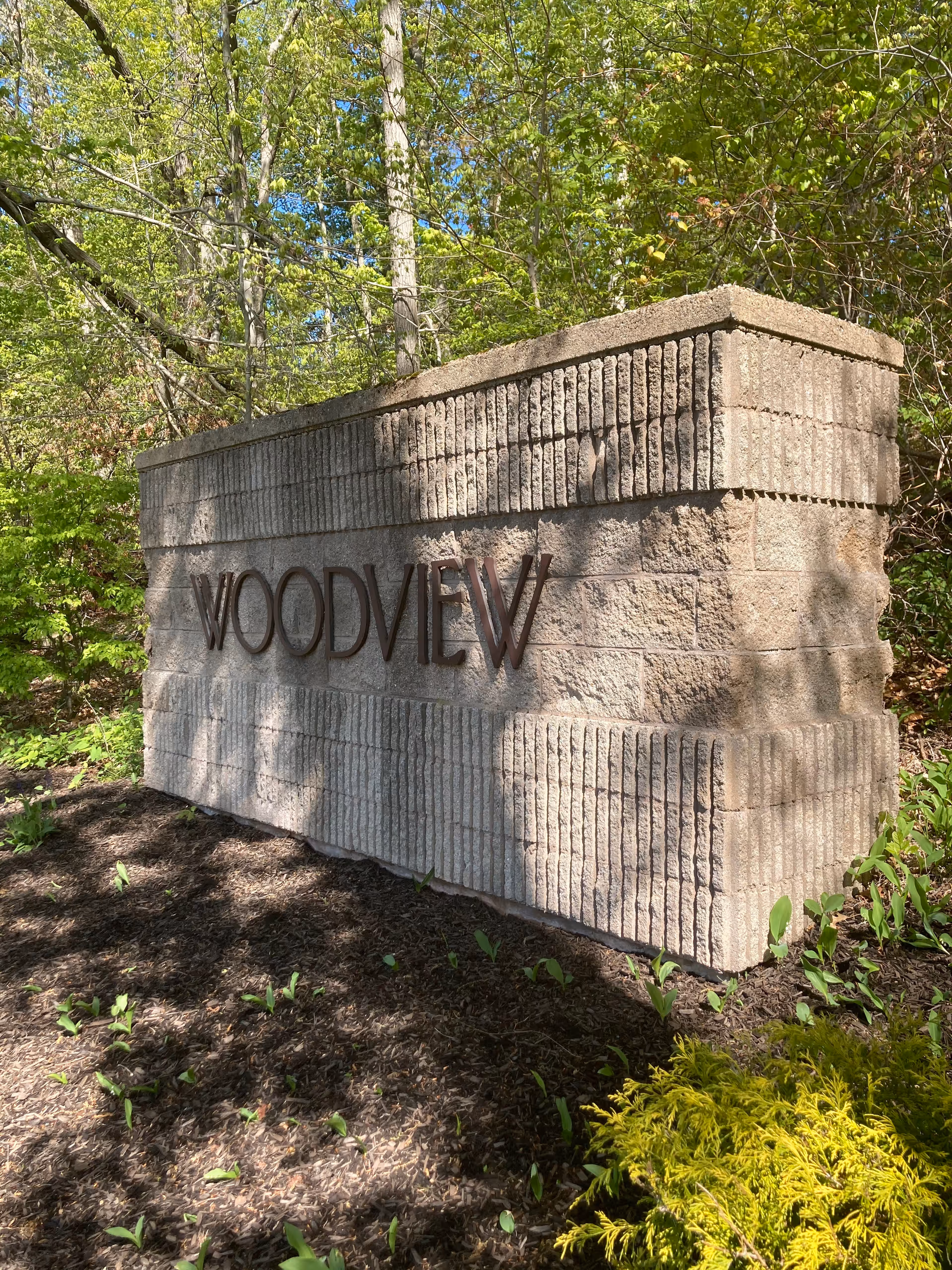 A large stone sign reading Woodview, set among trees with landscaped ground.