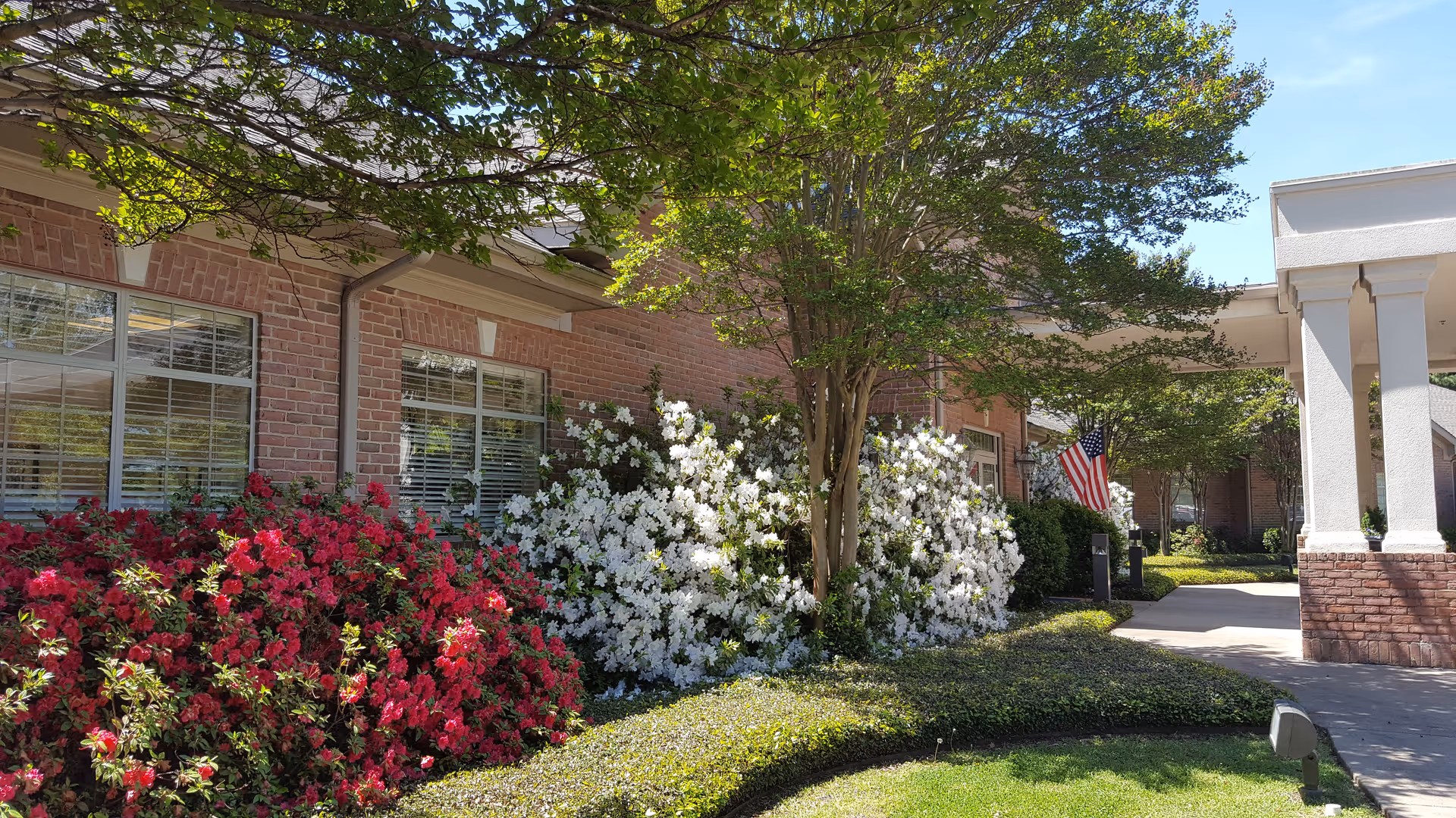 Front exterior of Hospice of East Texas with azaleas and a flag.