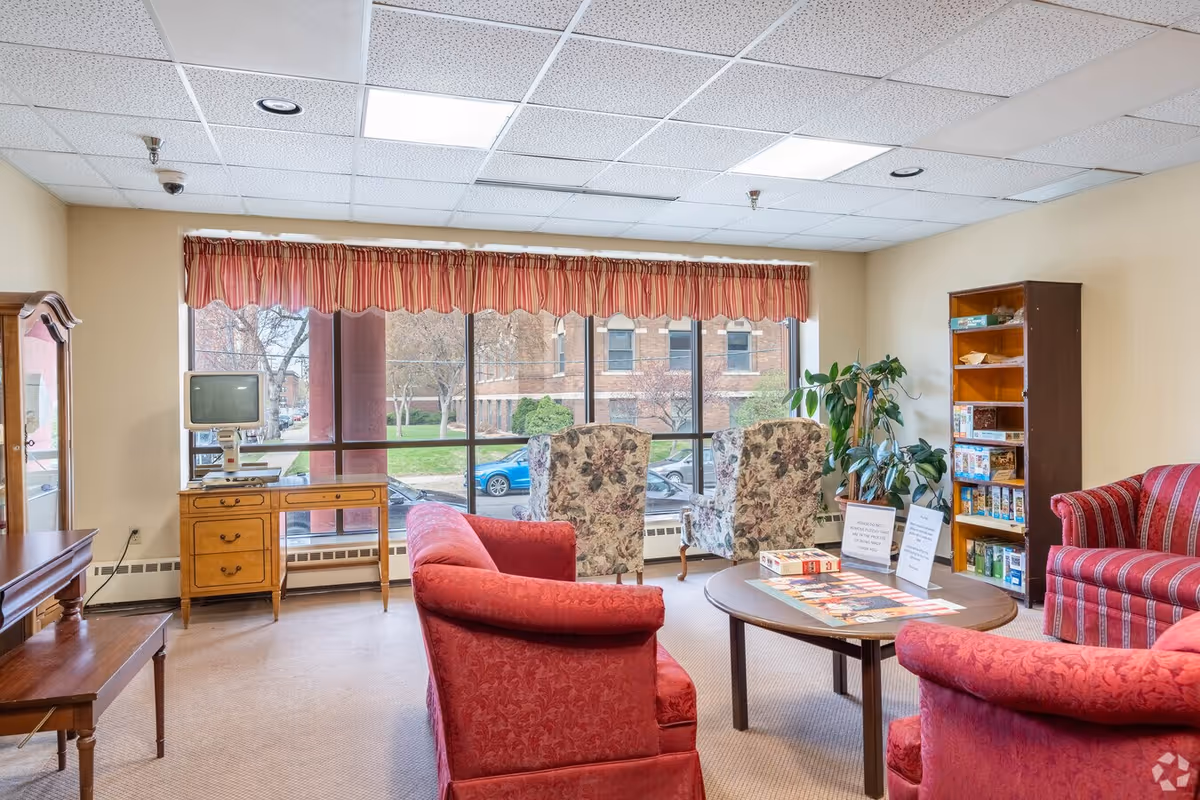 Lounge area in a senior living facility with red chairs and large windows.