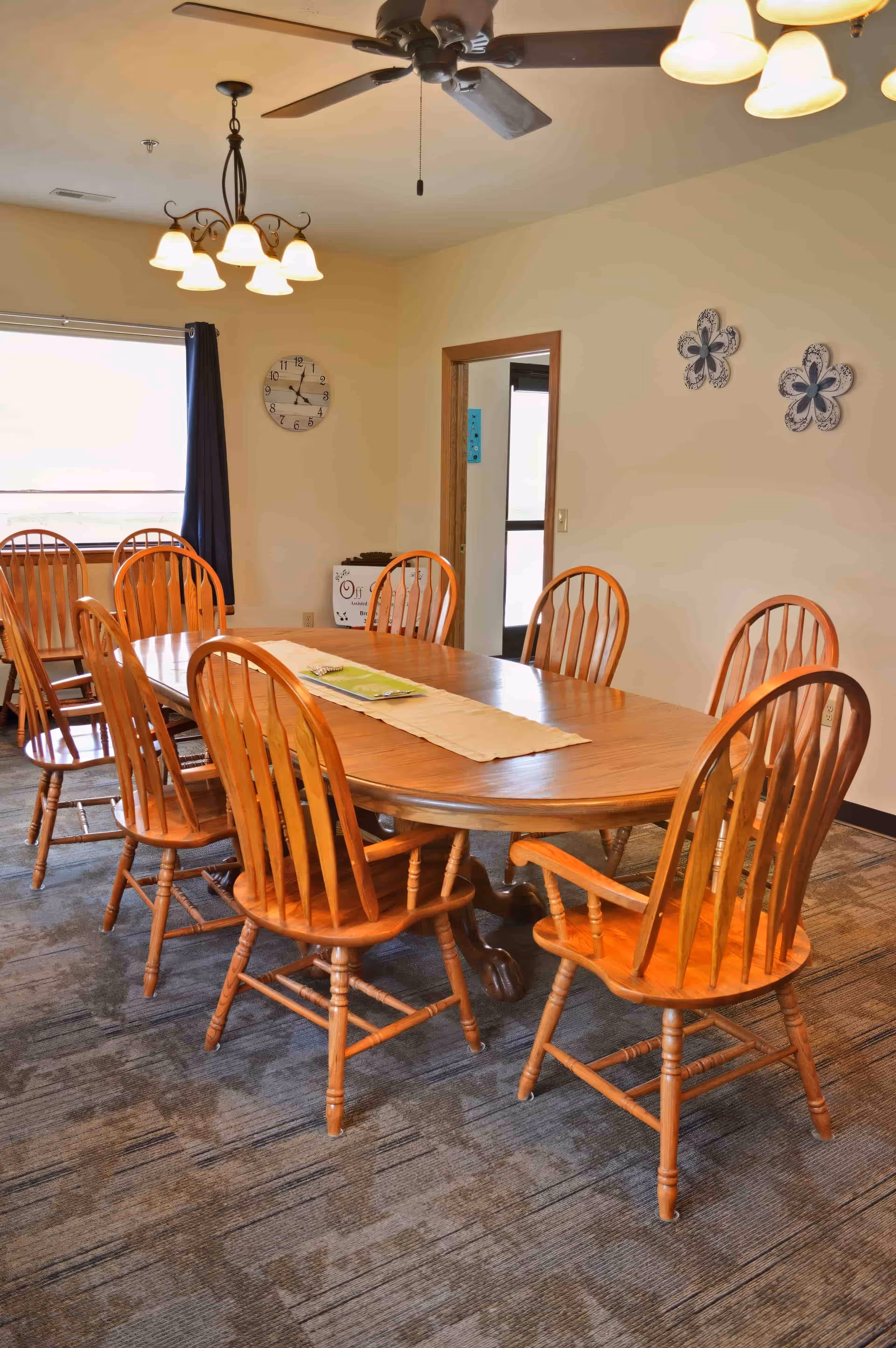 Dining room in senior living facility with a long wooden table, chairs, and overhead lights.