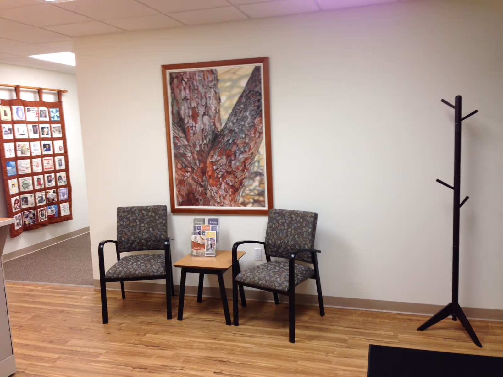 Two patterned chairs with a small table and a coat rack beside framed artwork.