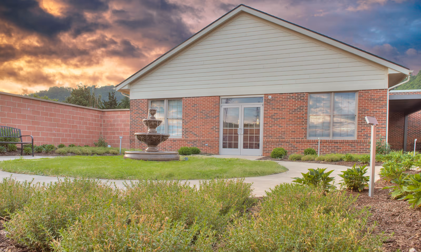 Front view of a brick building with a fountain and neatly landscaped surroundings.