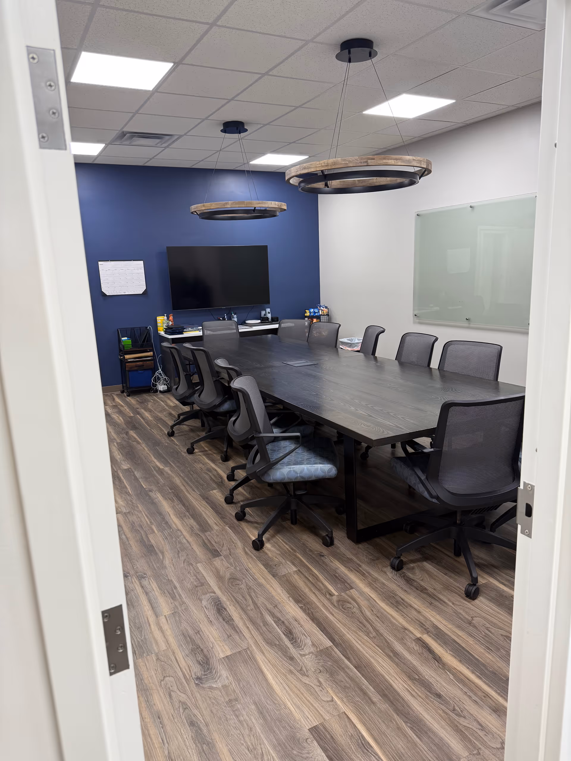 A modern conference room with a long table, chairs, a wall-mounted TV, and blue accent wall.