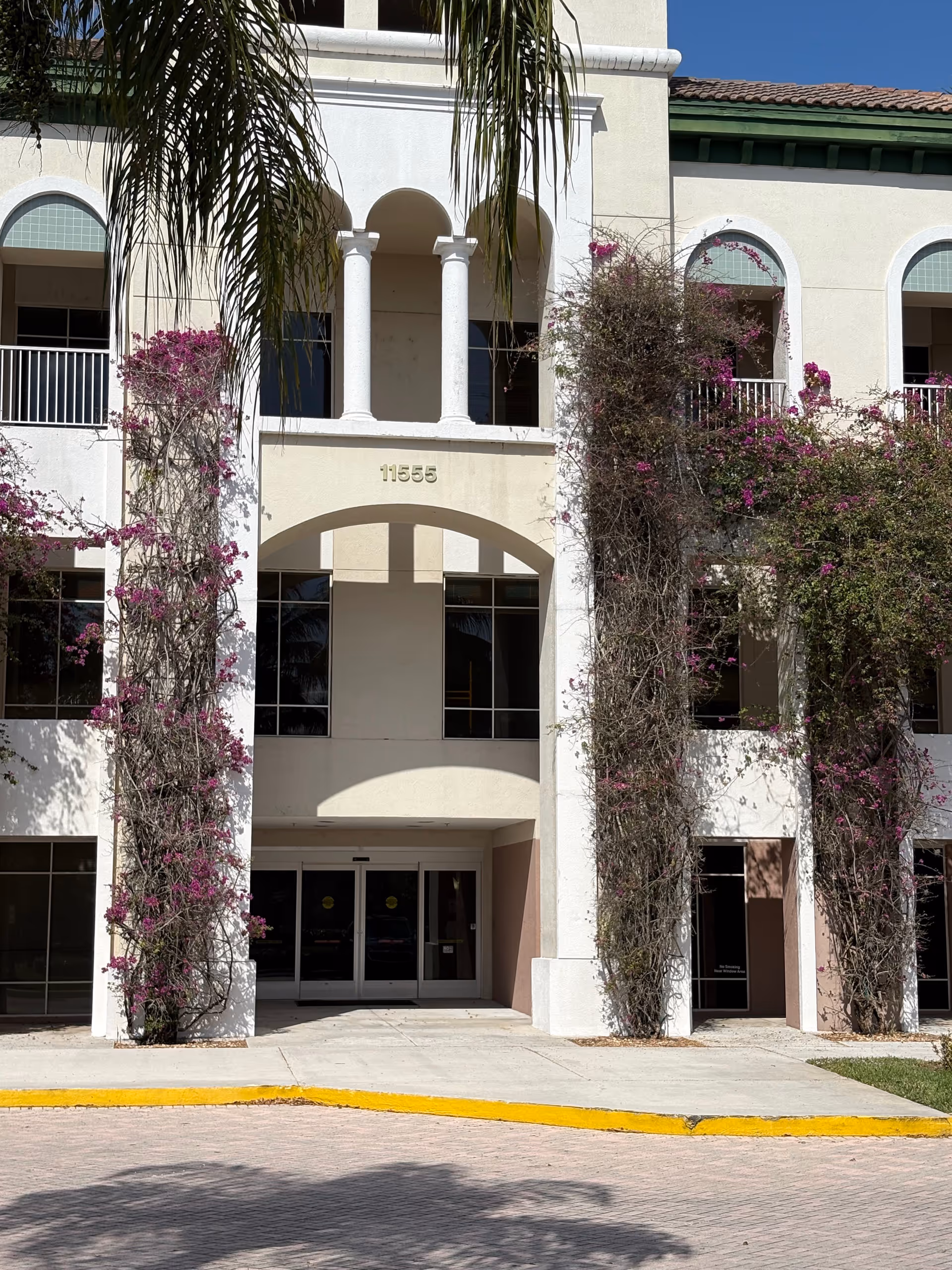 Exterior view of a senior living facility entrance with arches and flowering vines.