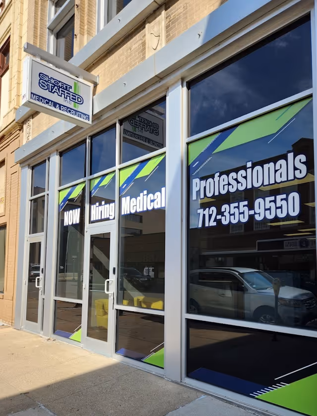 Exterior storefront with large windows advertising Now Hiring Medical and Short Staffed.