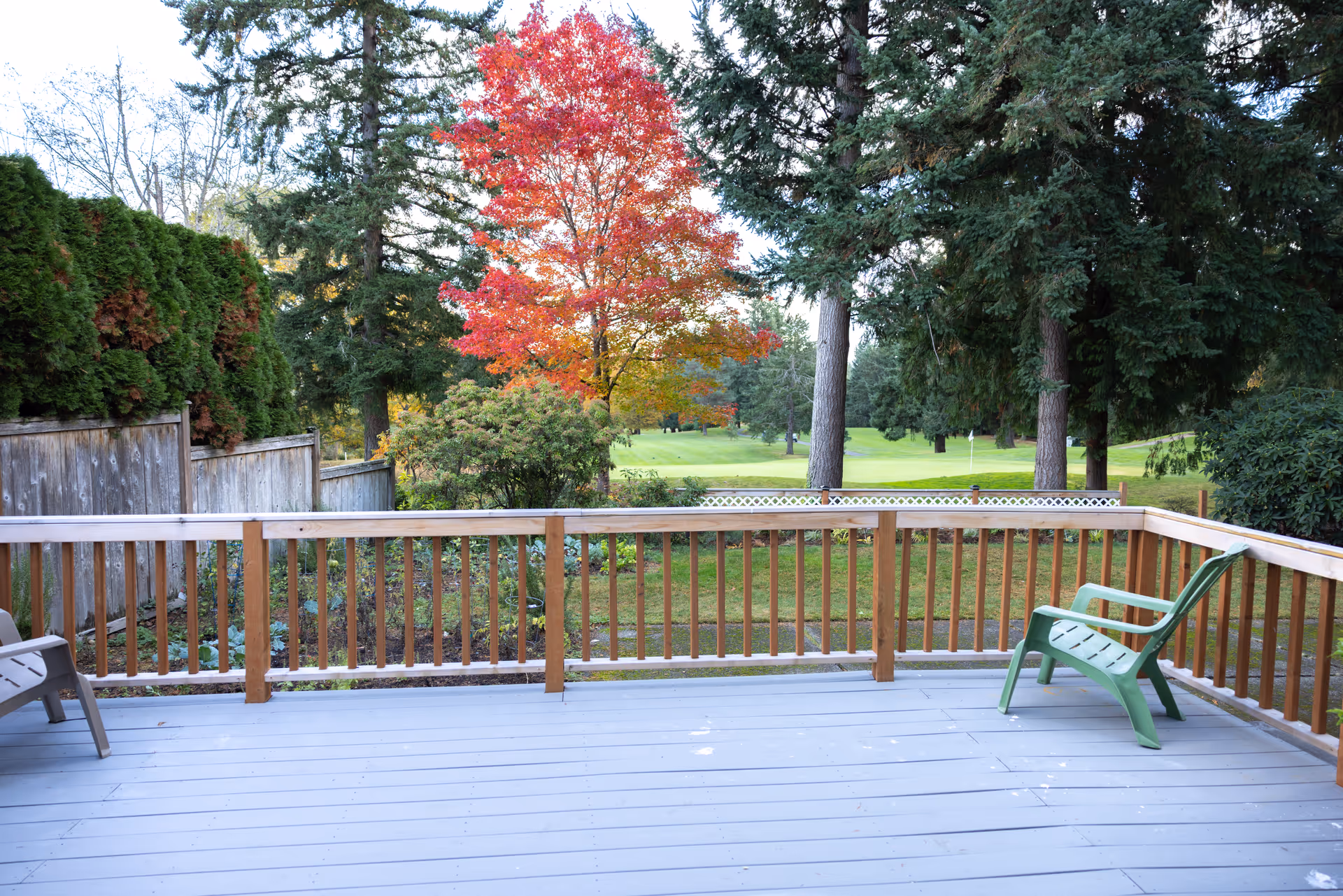 A wooden outdoor deck with plastic chairs overlooks a green yard and trees.