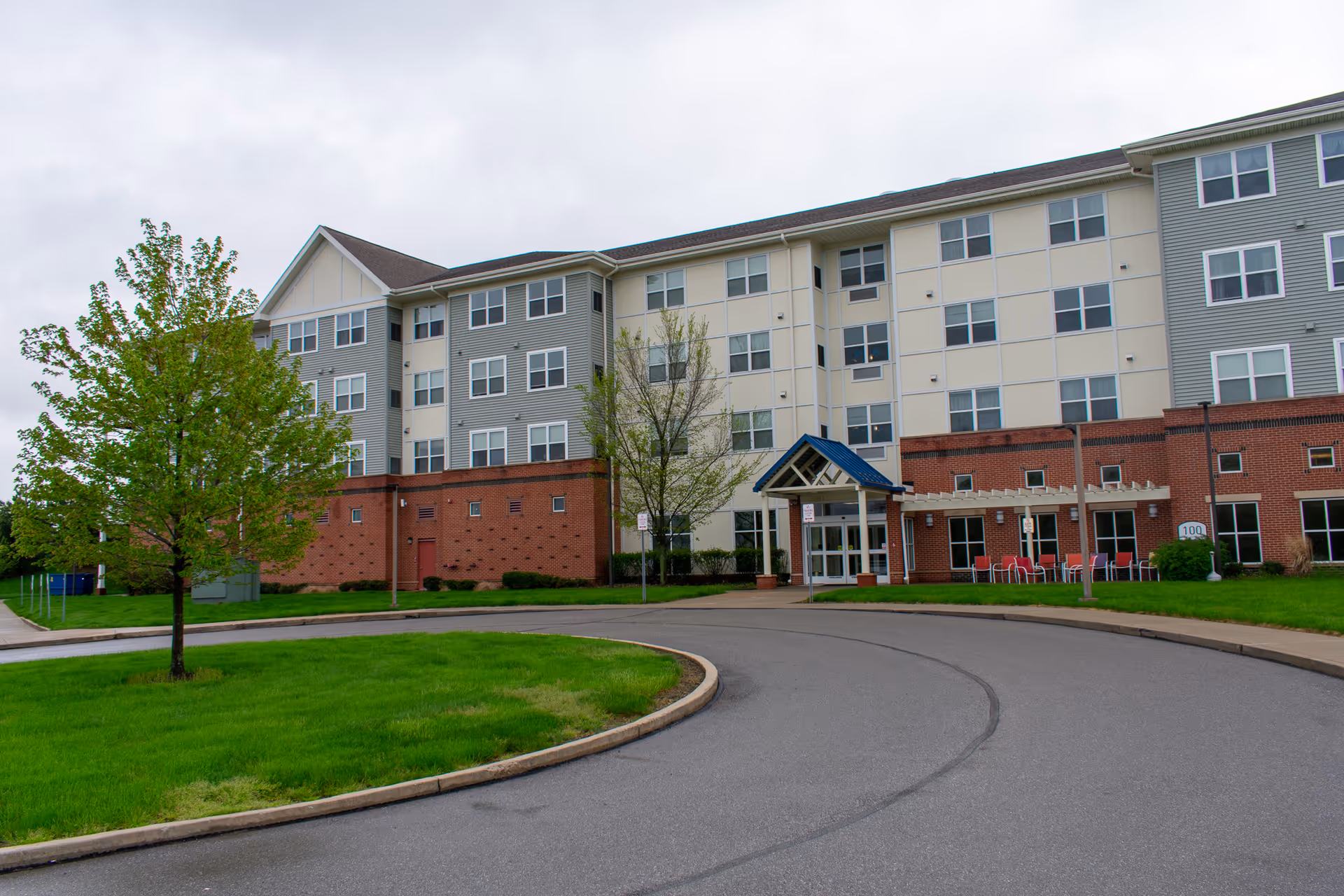 Exterior of a senior living facility with brick base, beige upper levels, and curved driveway.