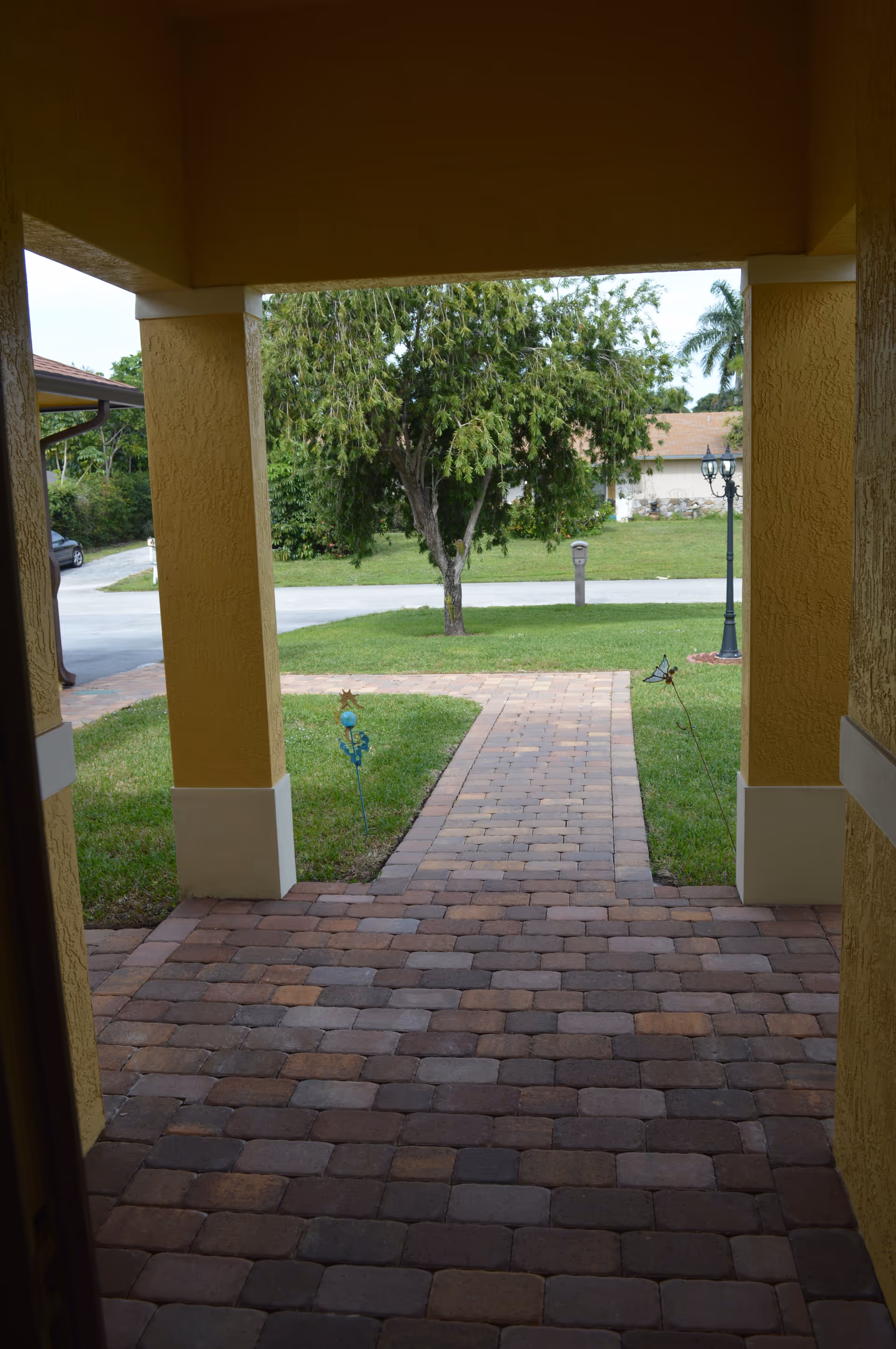 Covered yellow columns frame a brick walkway to a grassy yard and street.