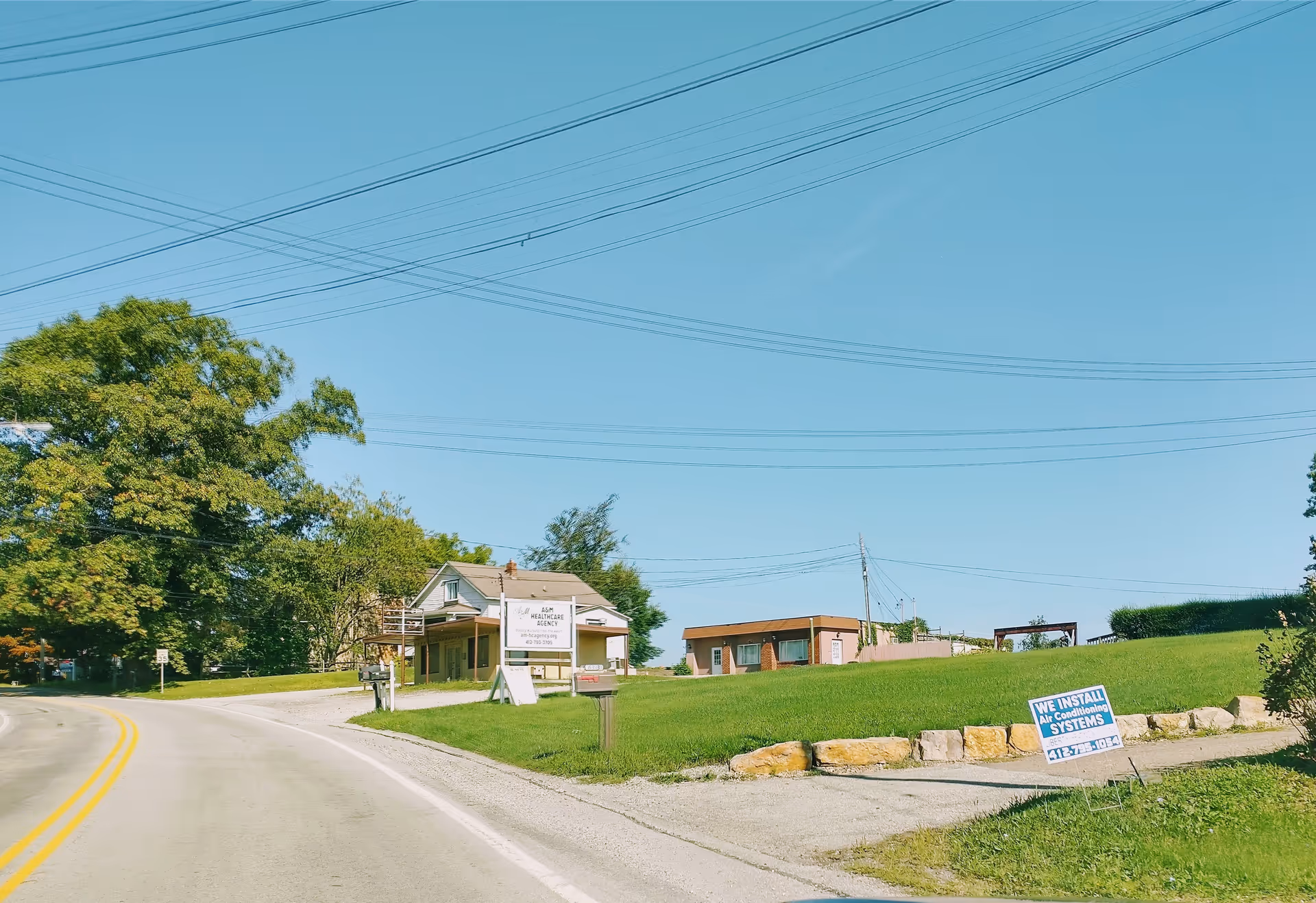 Road curves past a small building with a sign for A&M Healthcare Agency, LLC.