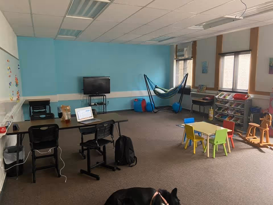 An indoor activity room with a small table, colorful chairs, a hammock, and a TV.