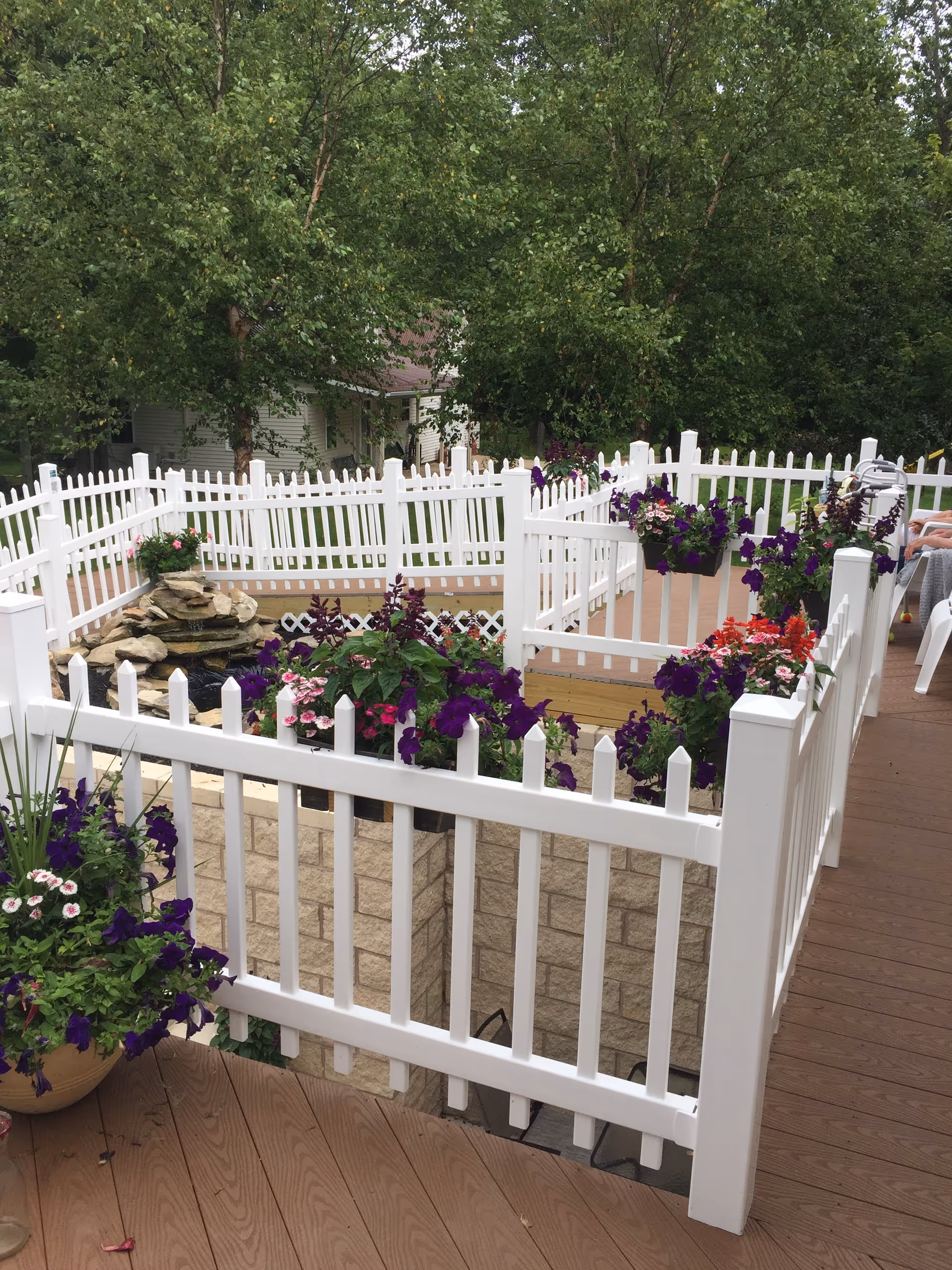 White picket fences surround a wooden deck with colorful flower planters.