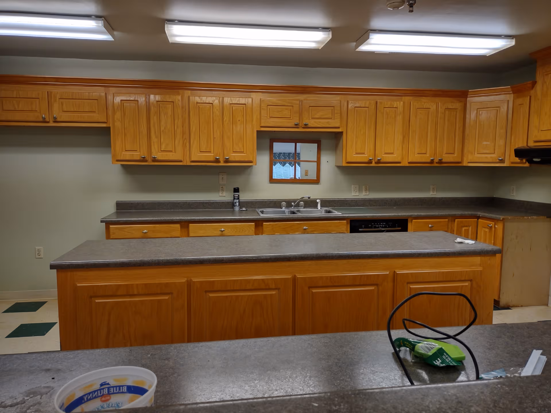 Senior living facility kitchen with wooden cabinets, countertops, island, and sink.