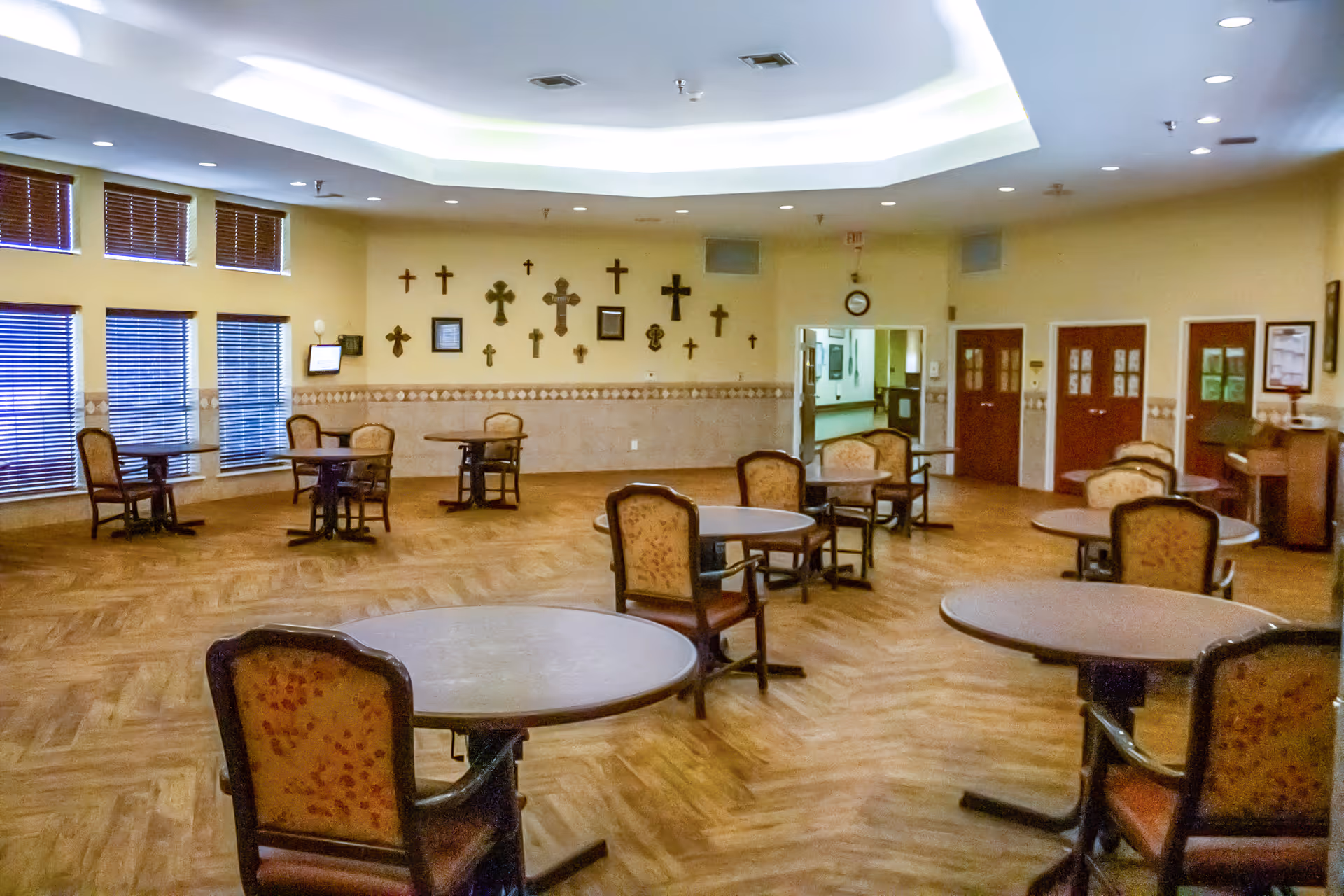 Spacious indoor dining area with round tables, cushioned chairs, and wall crosses.