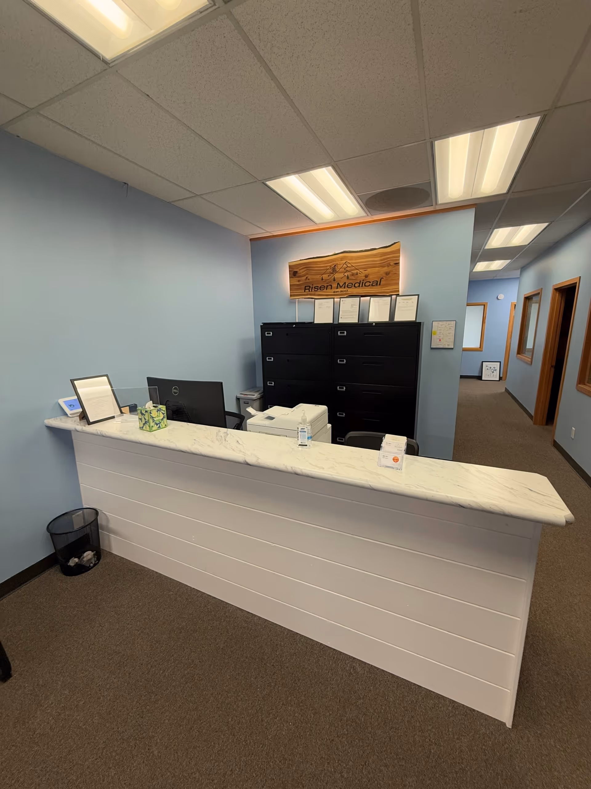 Reception desk with marble counter, printers, filing cabinets, and a sign reading Risen Medical Bend.