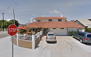 Exterior view of a two-story building with red tile roof, driveway, cars, and stop sign.