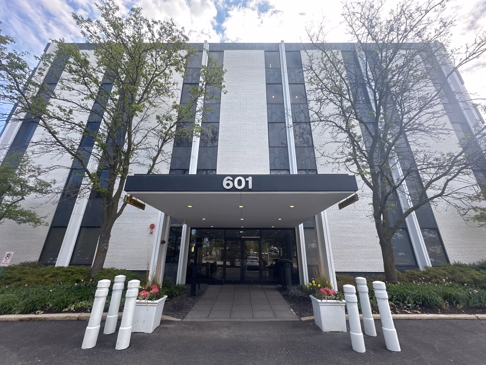 Modern six-story building front with a covered entrance labeled 601 and landscaped surroundings.