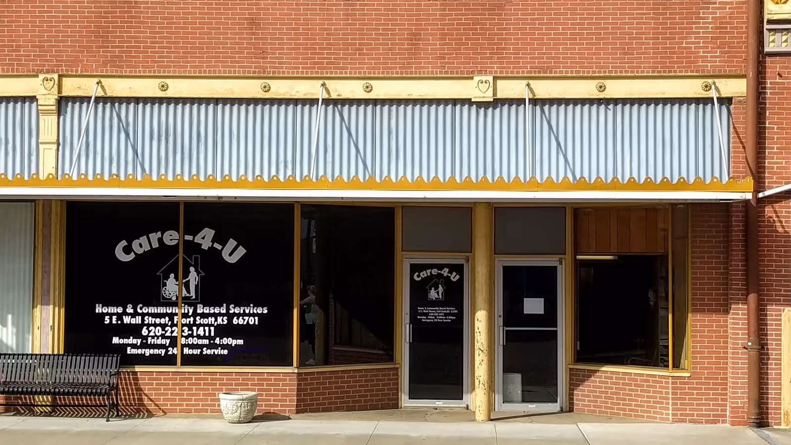 Brick storefront with Care-4-U signage, yellow awning, and glass doors outside.