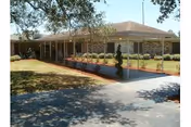 Exterior view of a single-story nursing home with a shaded front walkway and trees.