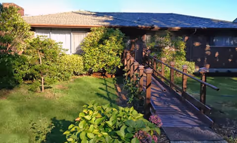 Exterior of Nurse Lavinia's Adult Family Home 2: wooden ramp entrance, green lawn, shrubs.