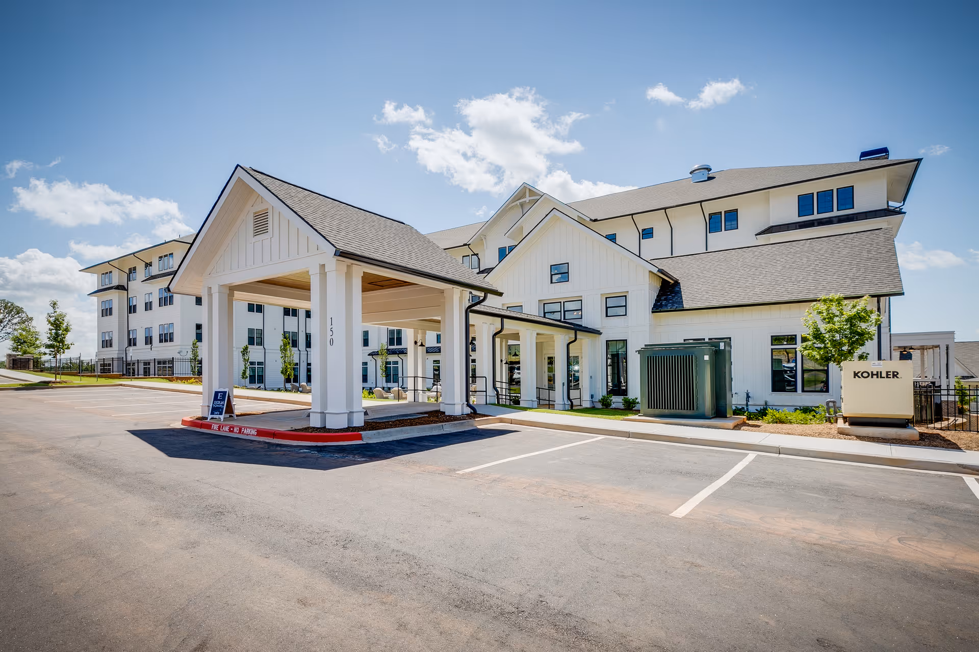 White modern senior living building with a covered entrance and parking in front