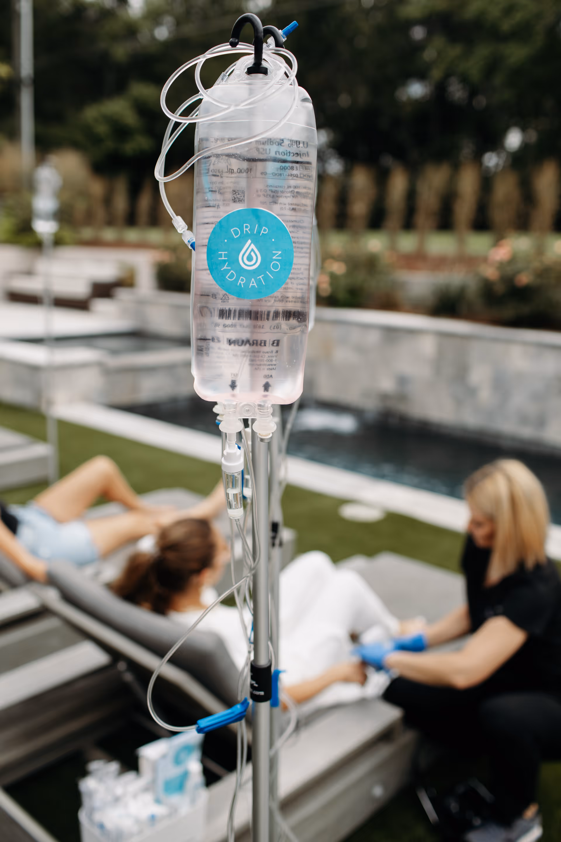 IV drip bag and tubing outdoors as two people receive mobile IV therapy.