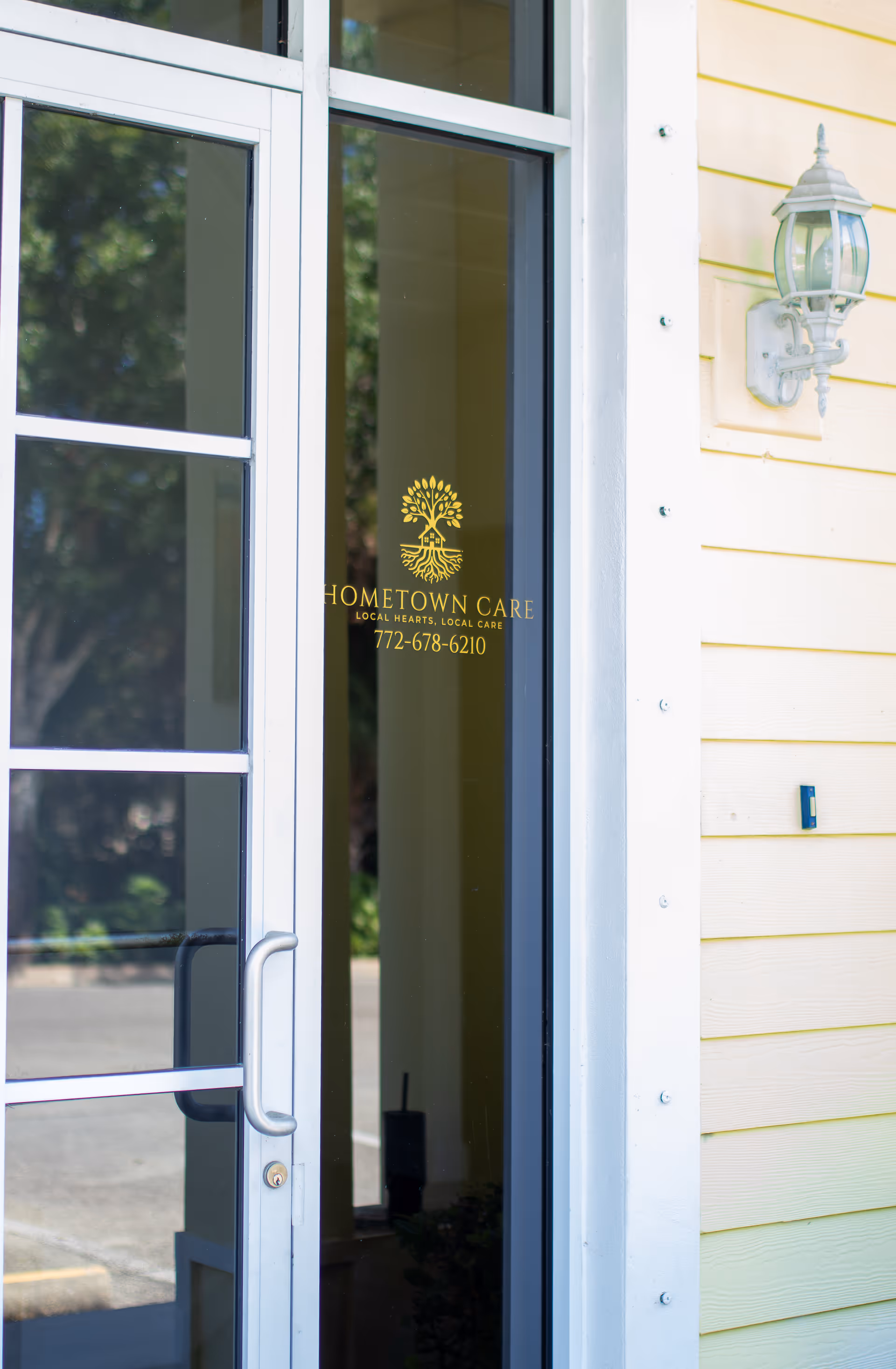 Glass door entrance bearing Hometown Care logo and gold lettering, with beige siding and wall light.