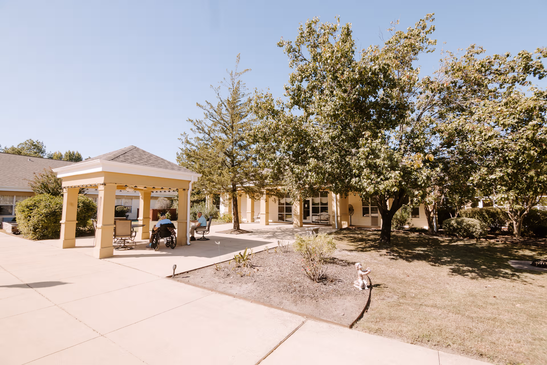 Outdoor courtyard of a senior facility with a shaded pavilion and residents seated.