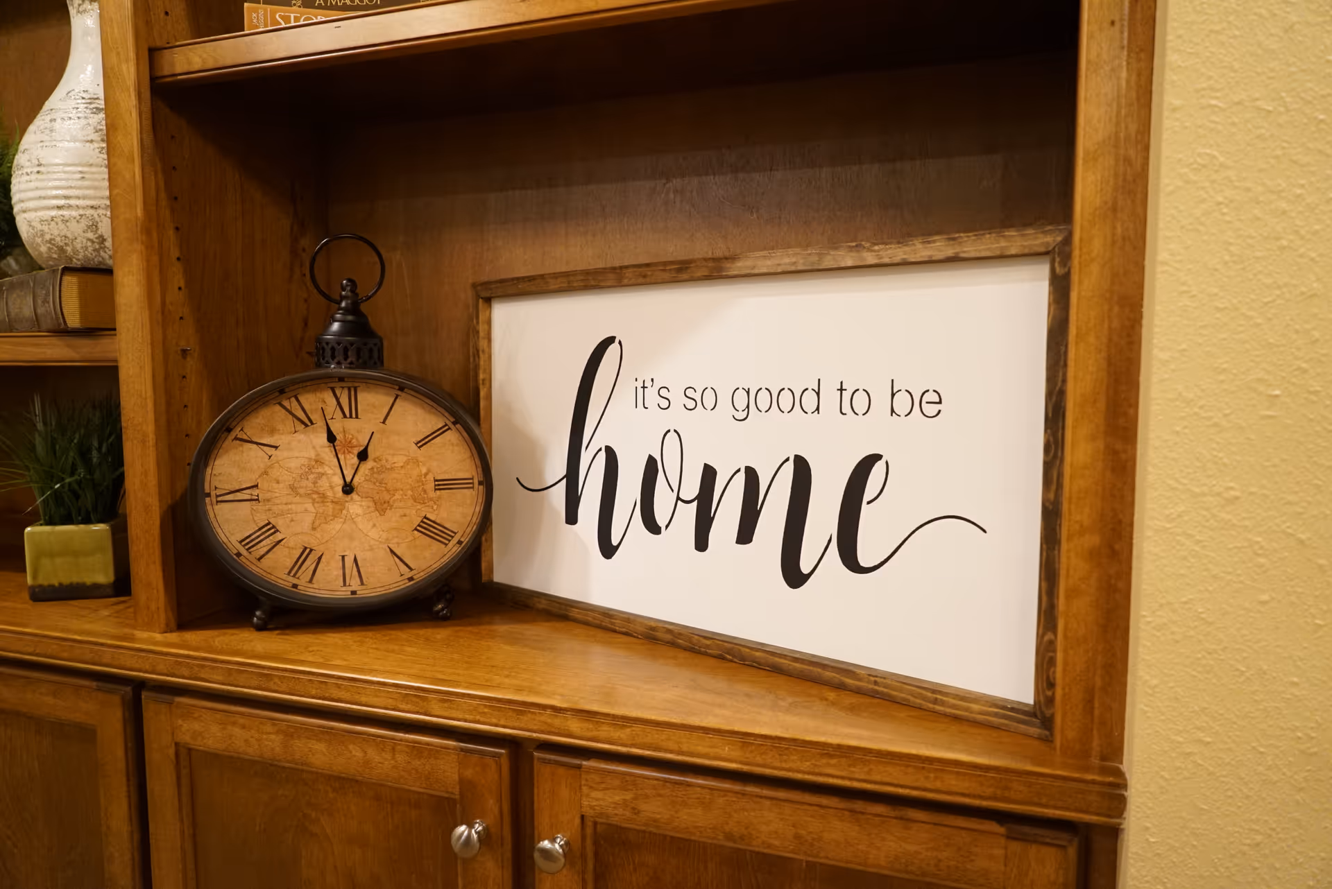Wooden cabinet with a vintage clock and framed home sign on a shelf.