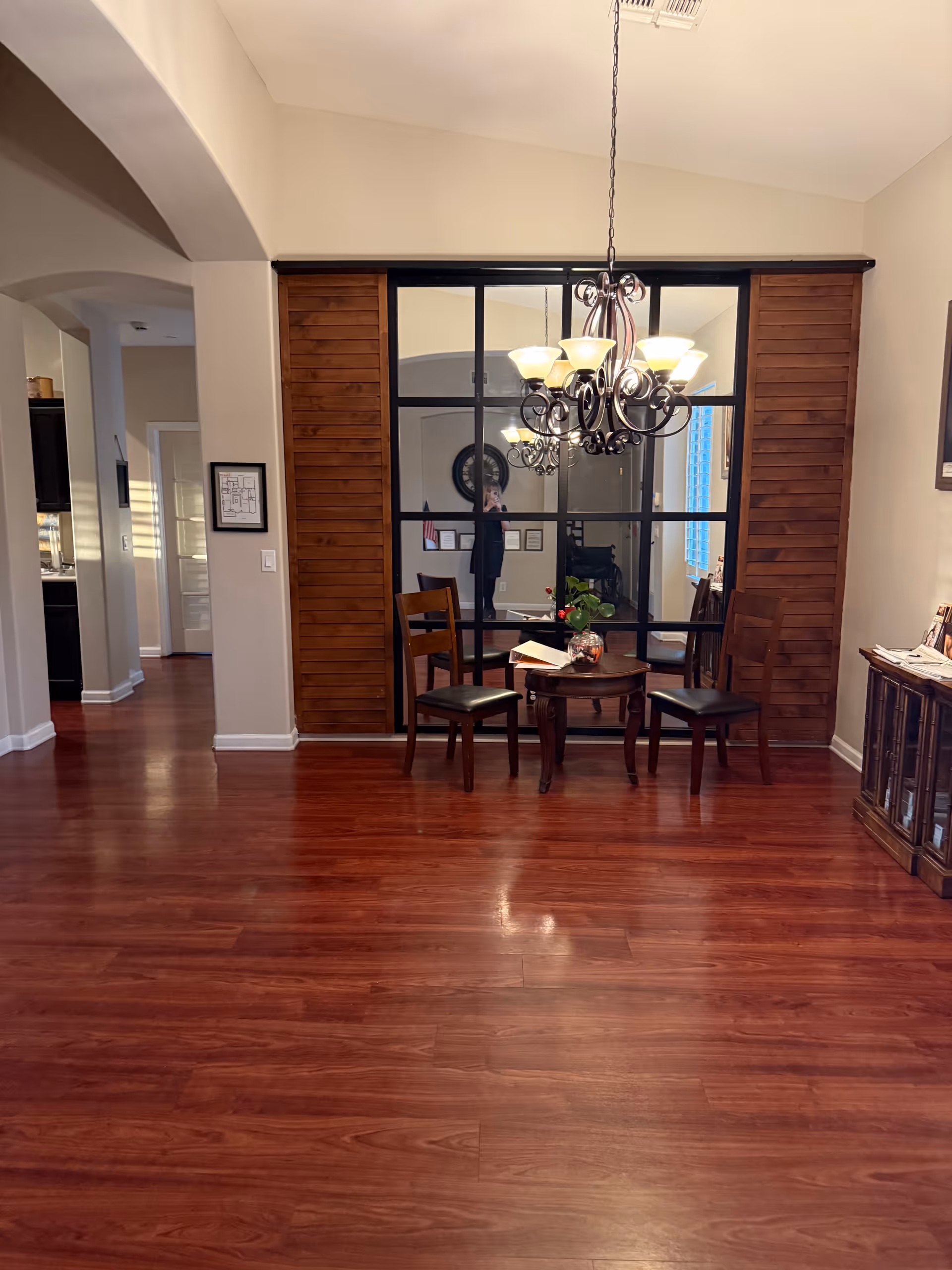 Spacious interior with wooden floor, glass partition, chandelier, and small dining table.