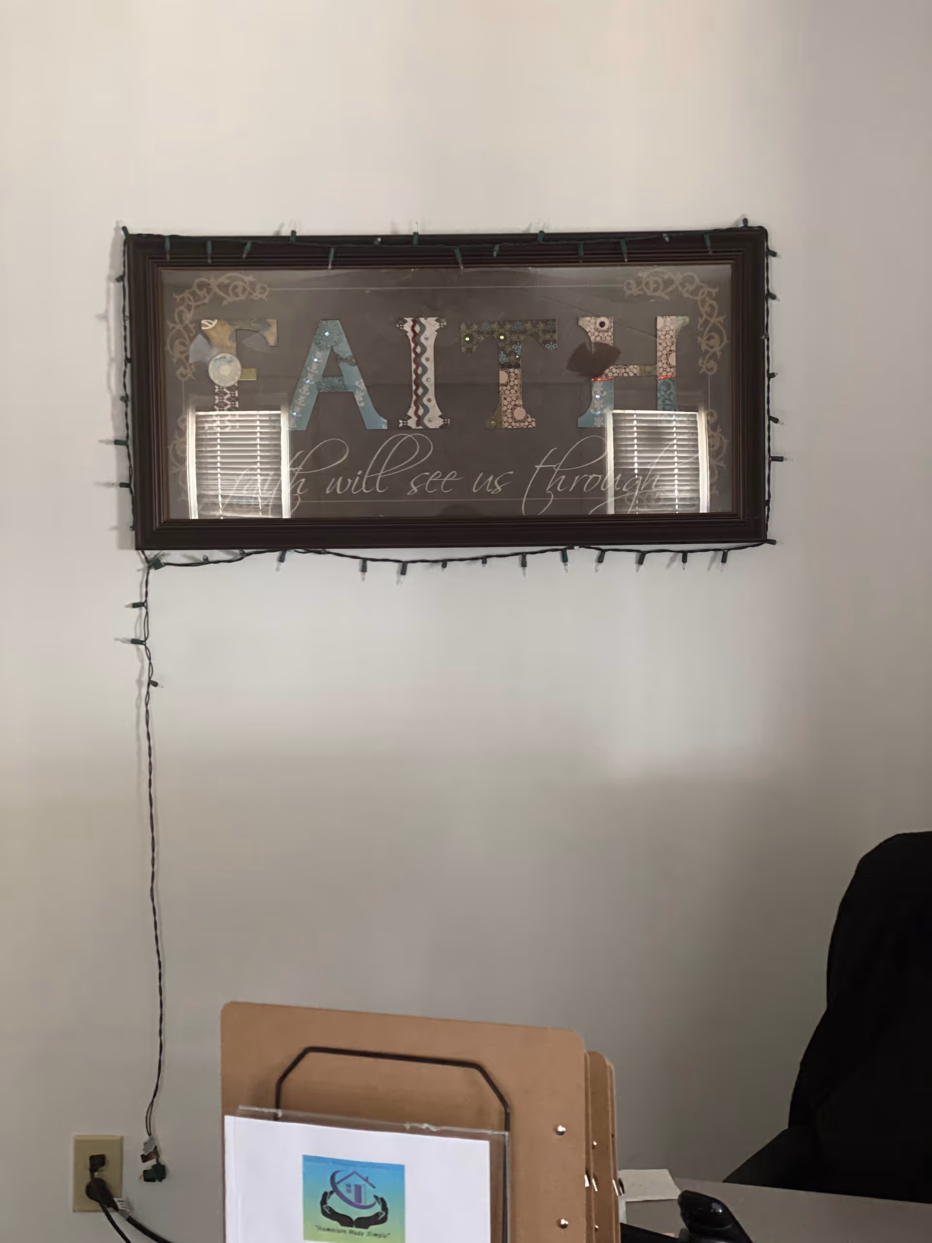 Interior office area with a framed 'FAITH' sign, string lights, and desk with folders.