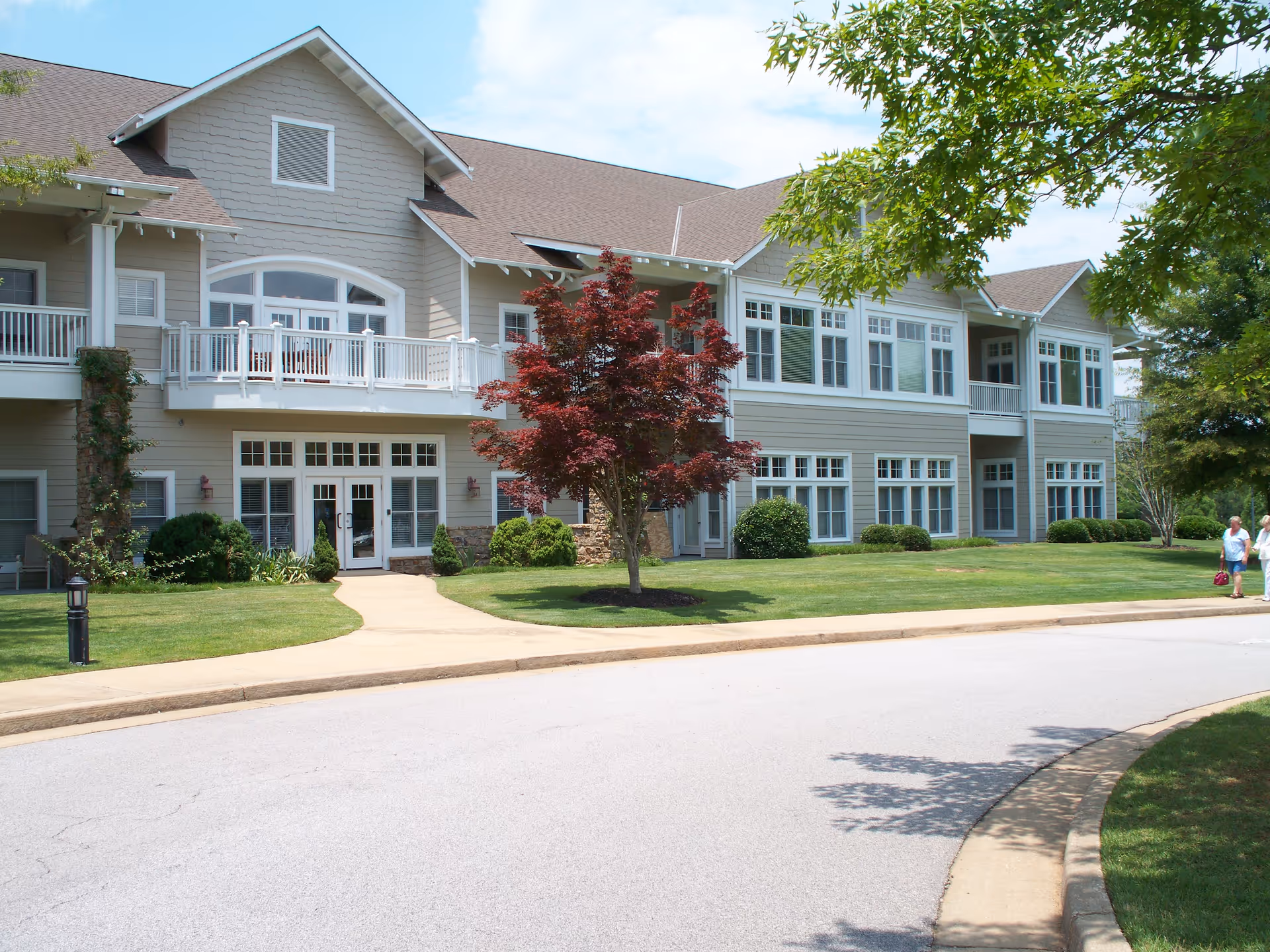 Vernon Woods senior living building with balconies, lawn, and tree-lined sidewalk.