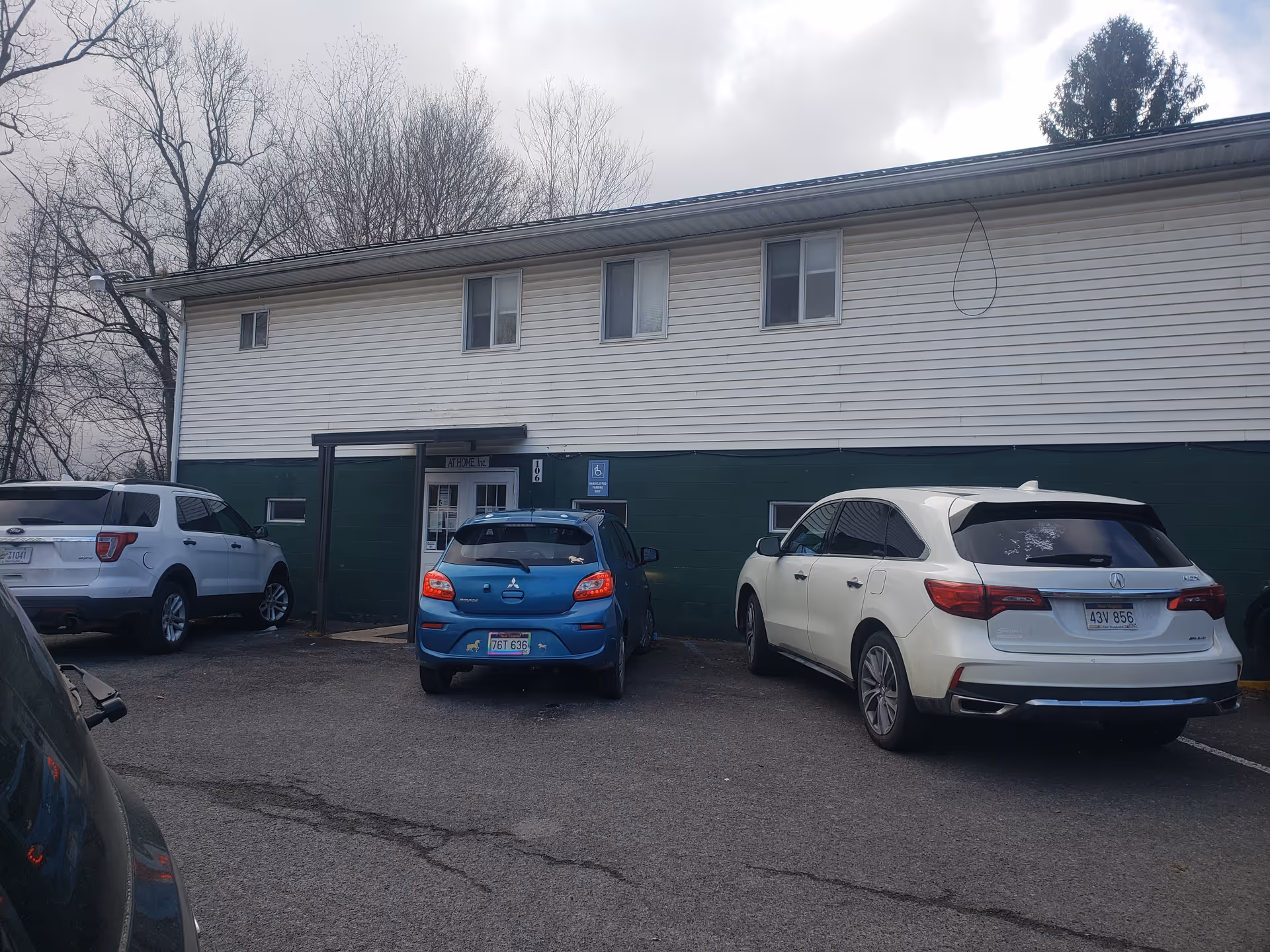 Front view of a two-story building with white siding, a green base, and parked cars.