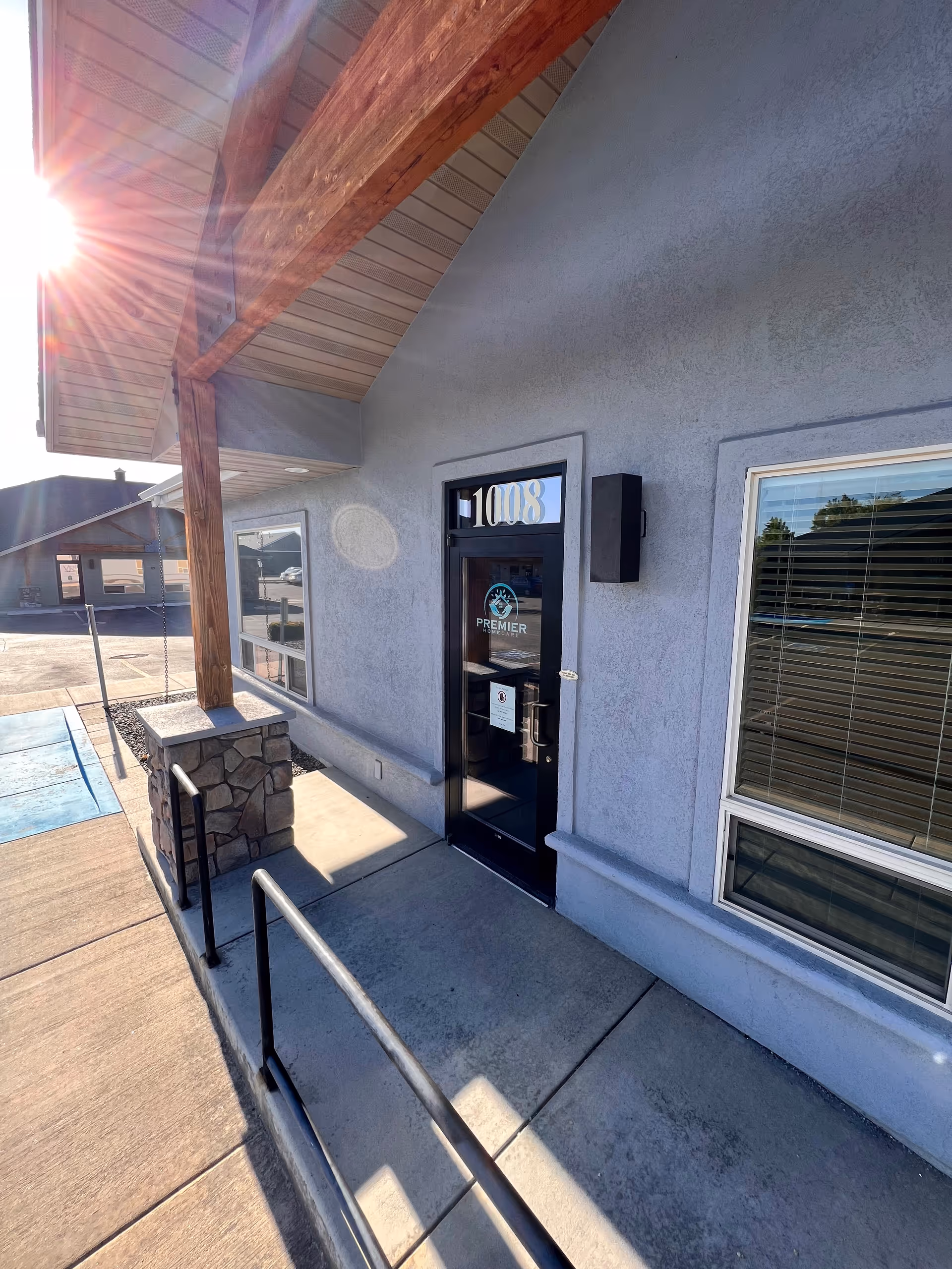Sunlit exterior view of Premier Home Care entrance with glass door and ramp