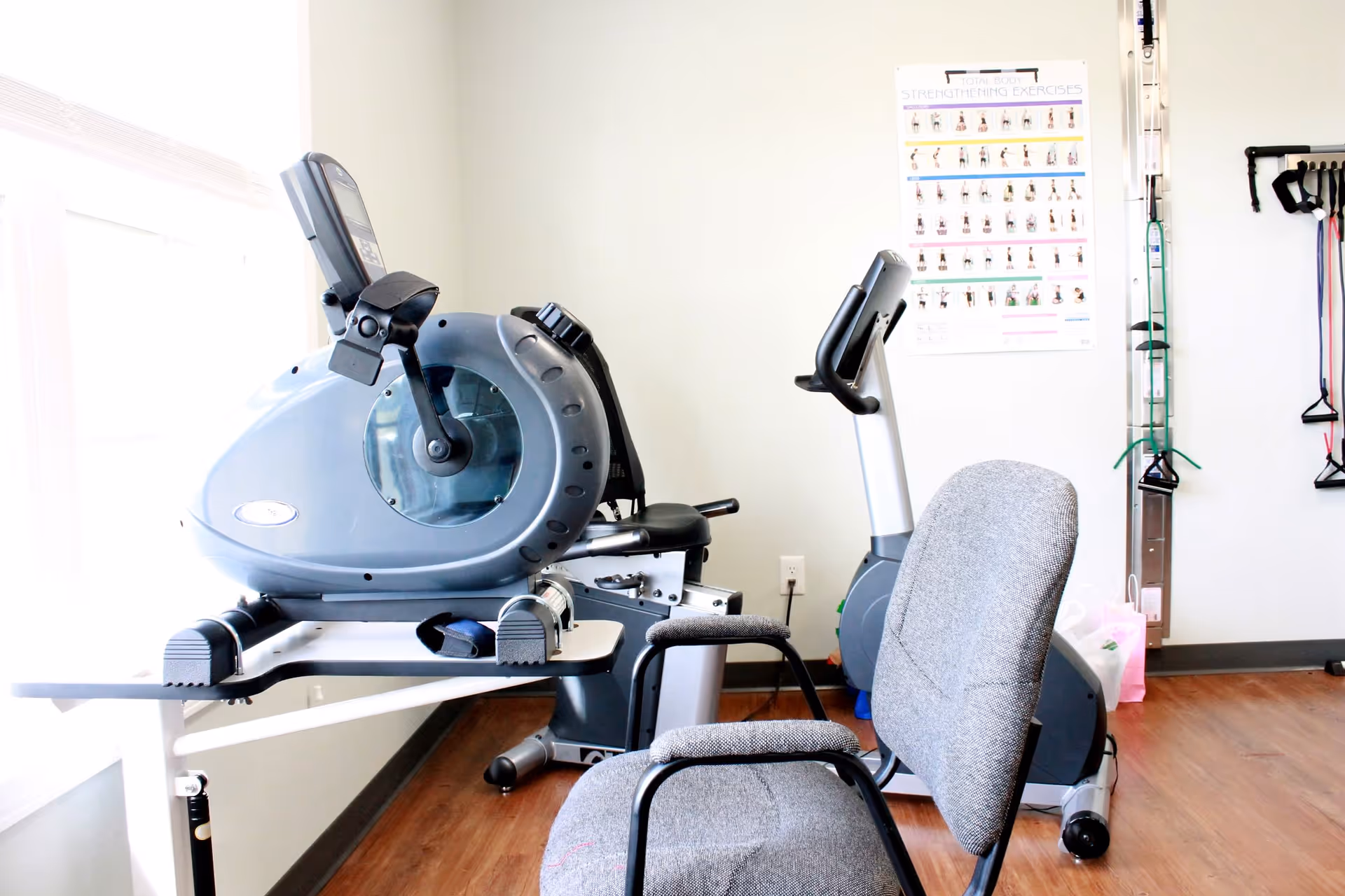 A fitness room featuring exercise equipment, including a stationary bike and an elliptical machine, with a poster of strengthening exercises on the wall.