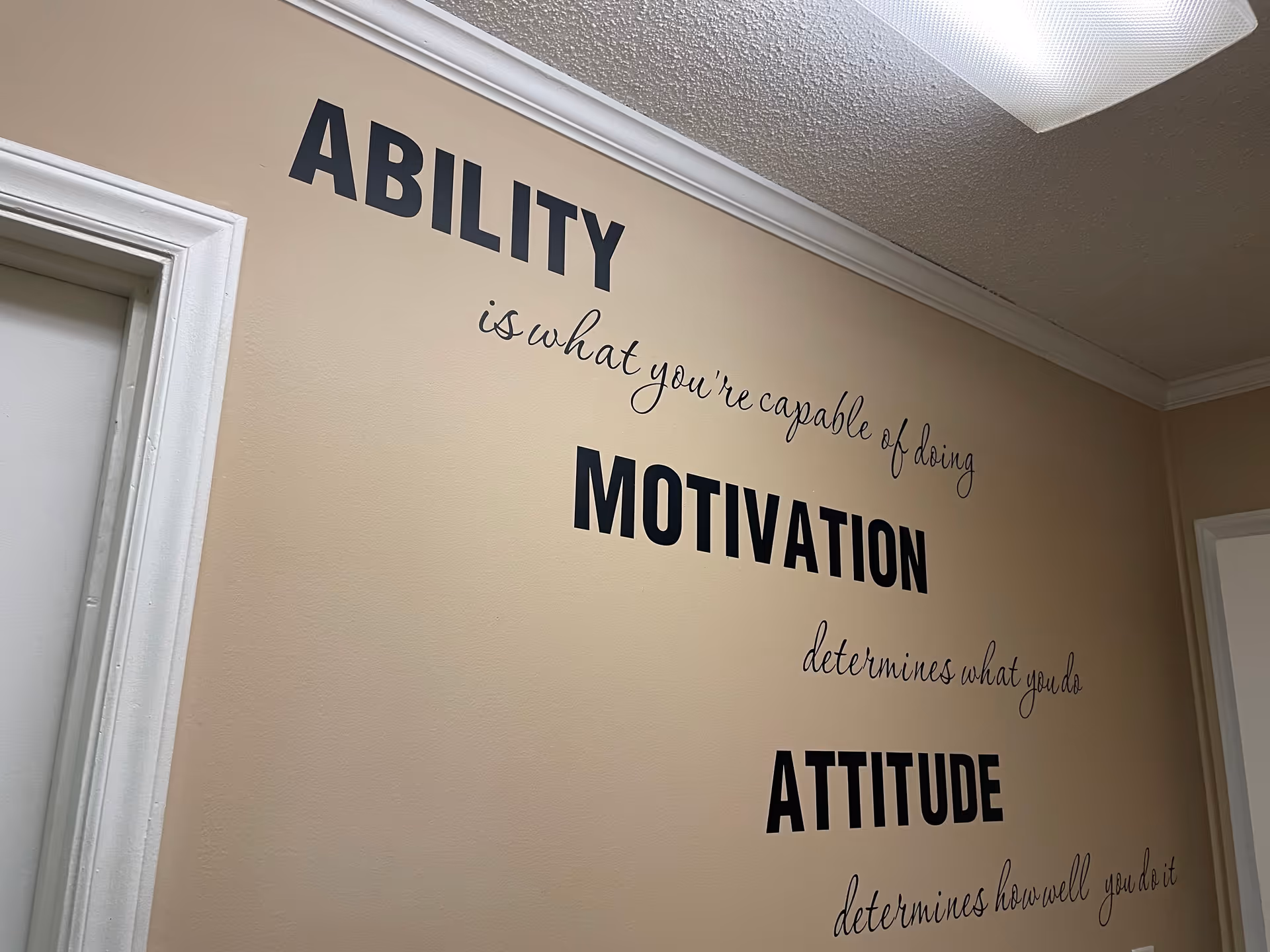 Beige interior wall with large motivational quotes reading 'Ability', 'Motivation', and 'Attitude'.