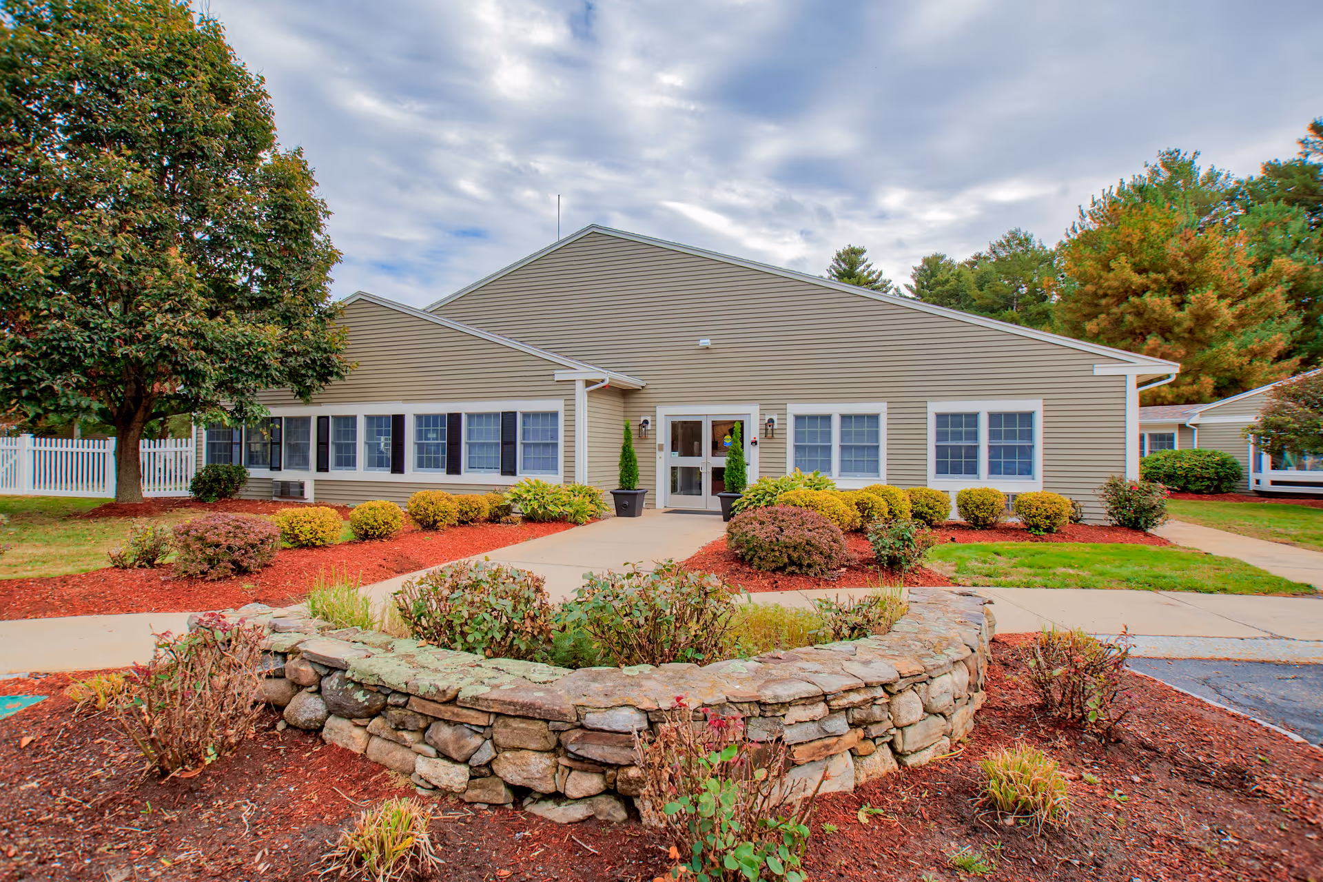 Single-story beige senior living facility with front entrance and landscaped circular stone planter.