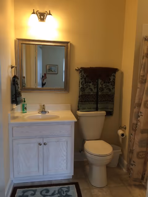 Bathroom with sink vanity, mirror, toilet, and towels in a senior living facility.